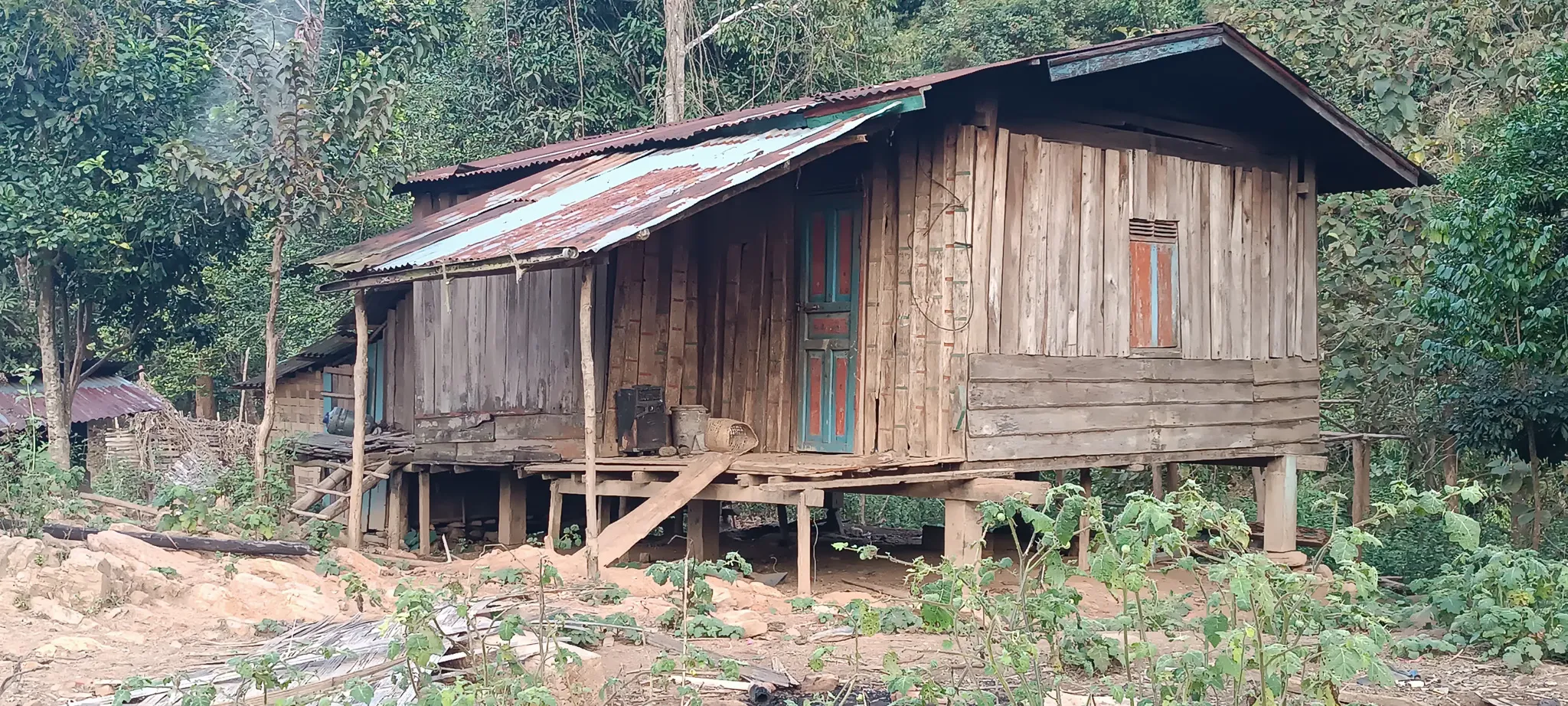 Close-up of a deteriorating wooden stilted house with rusty tin roof at an abandoned settlement beside the Nam Ou river