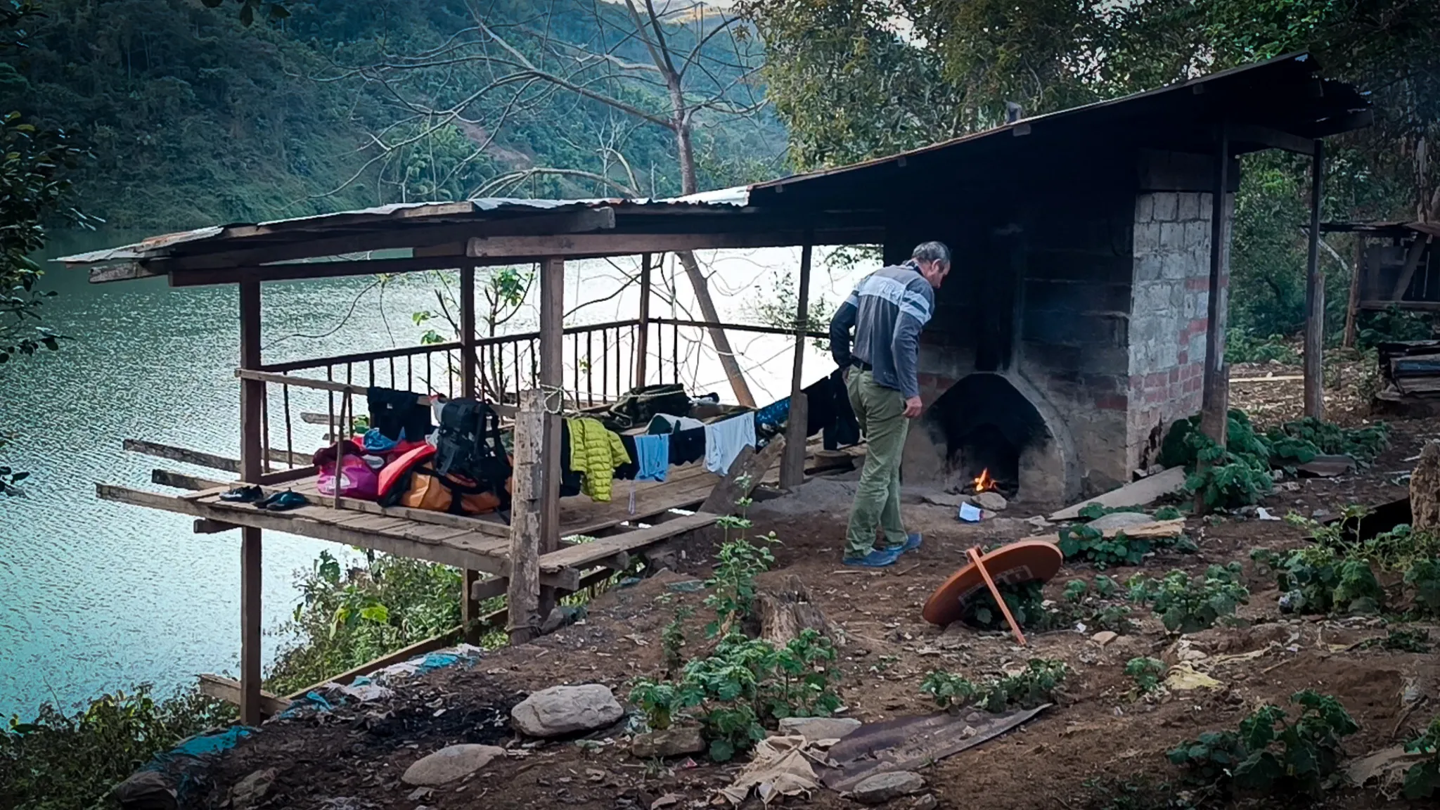 Abandoned open shelter with corrugated roof and brick oven being used as a campsite beside the Nam Ou river at dusk