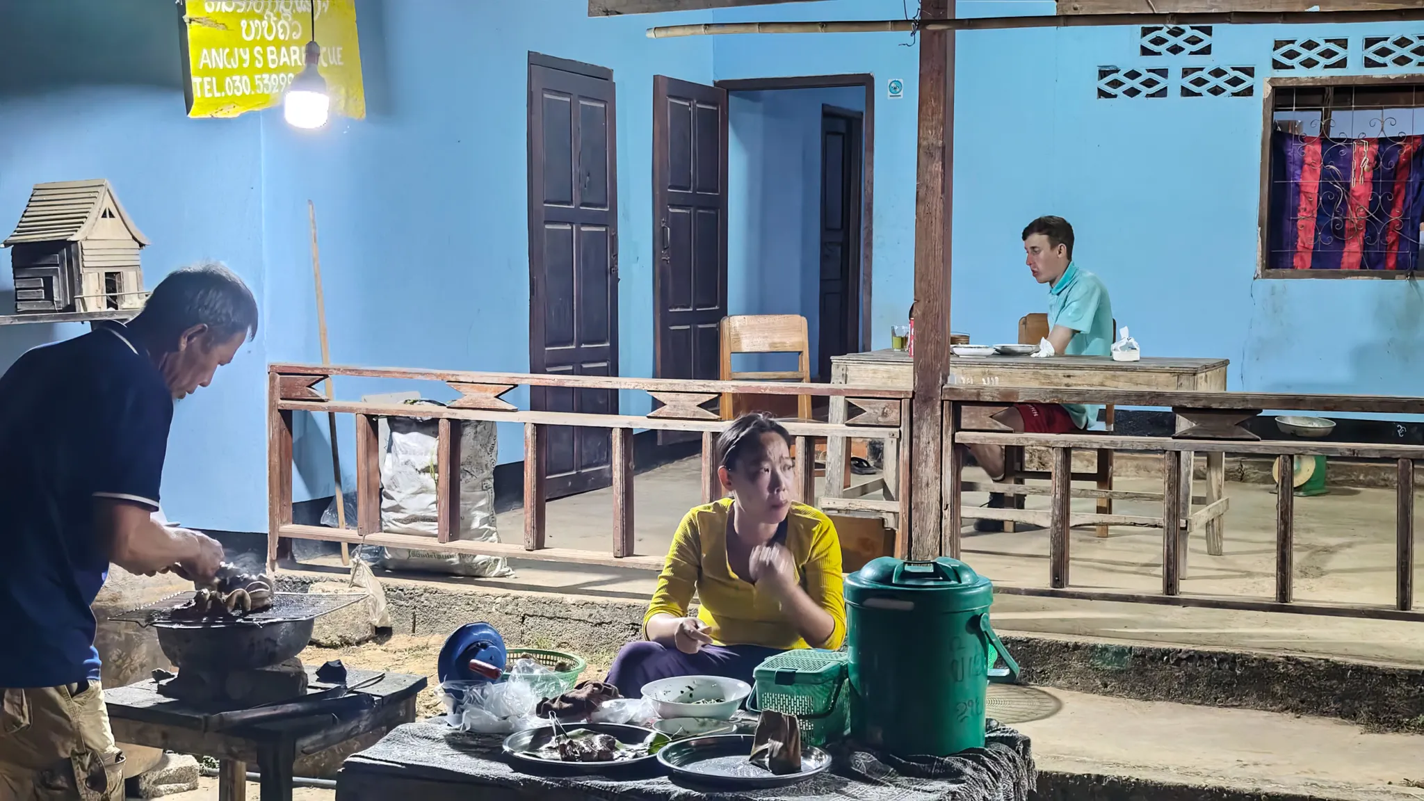 Angee's BBQ stand at night in Muang Ngoi with a lady grilling meat and a woman seated nearby