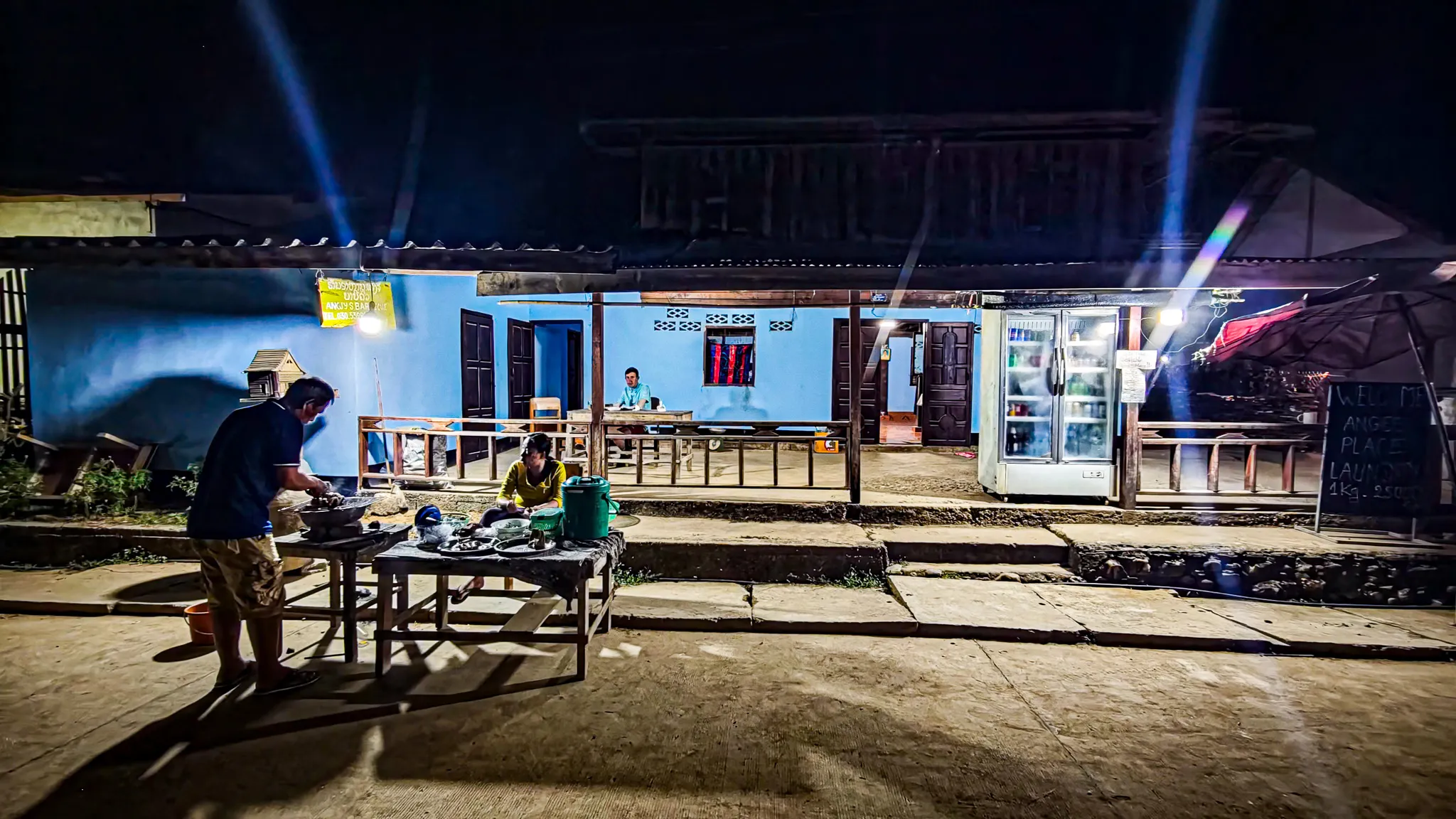 Wide view of Angee's BBQ street food stall lit up at night on the main strip of Muang Ngoi