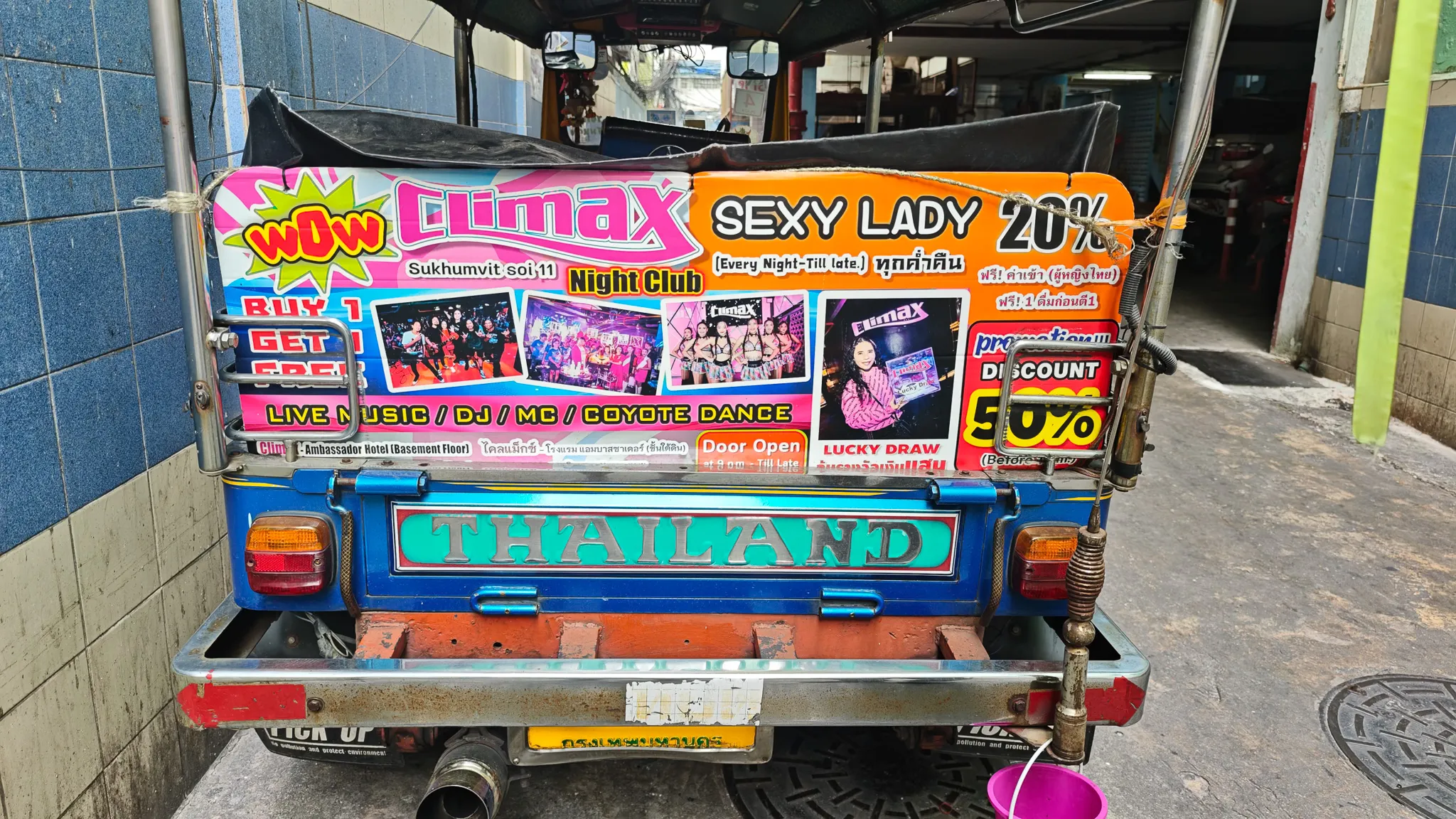 Colourful rear of a Bangkok tuk tuk covered in nightclub advertisements in a narrow soi