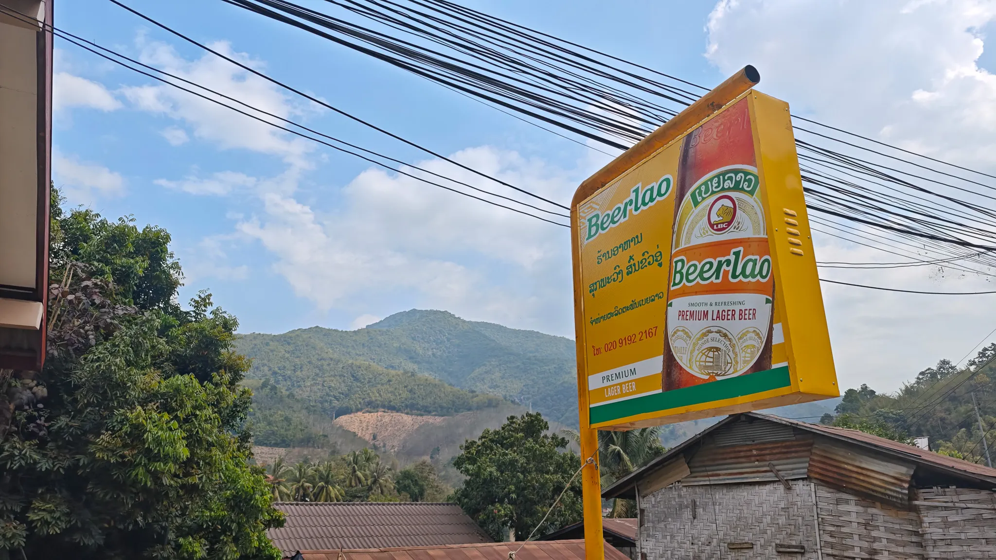 Beerlao advertising sign against a backdrop of green mountains and power lines in Muang Khua, Laos