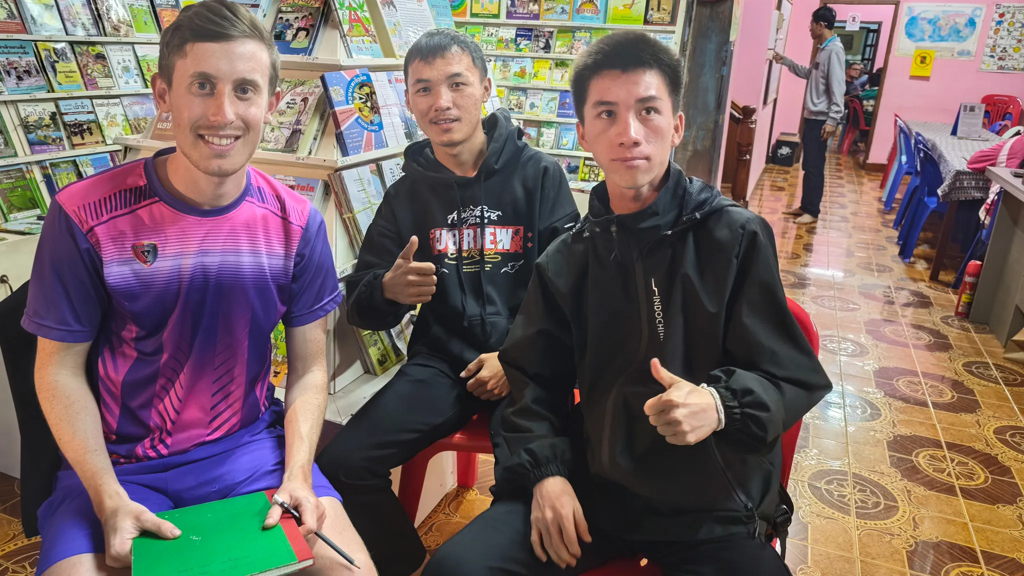 Volunteer posing with Sing and Ying from the Mong ethnic group at Big Brother Mouse library with bookshelves in the background