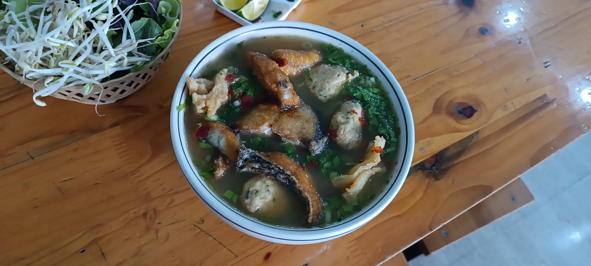 Bowl of bun ca fish soup with fried fish pieces, herbs and chilli served with fresh bean sprouts in Dien Bien Phu