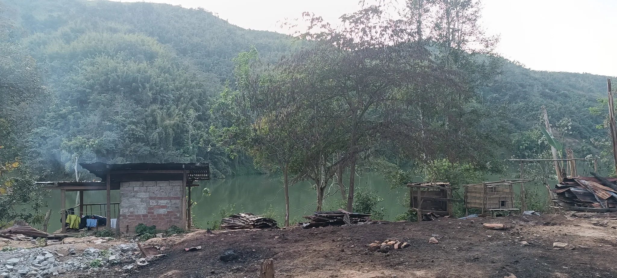 The abandoned settlement shelter and surrounding derelict structures being used as a campsite overlooking the Nam Ou river and mountains