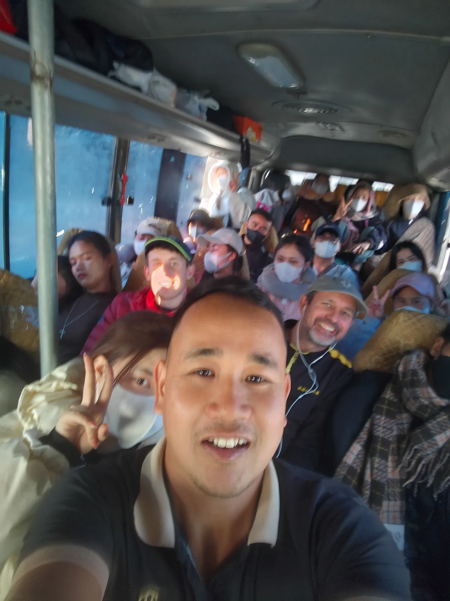 Group selfie inside the packed 33-person bus from Dien Bien Phu heading towards the Laos border, passengers wearing face masks