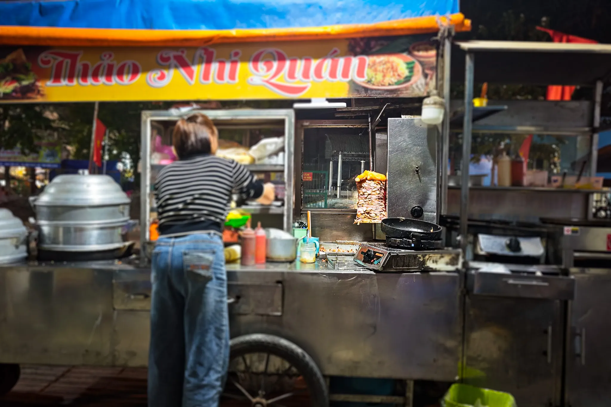 Street food vendor at Thao Nhi Quan stall in Dien Bien Phu serving donner kebab banh mi from a rotating meat spit