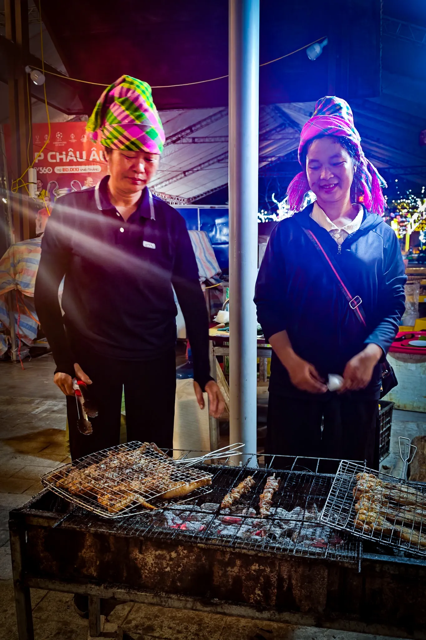 Vietnamese couple grilling lamb and pork skewers at the Dien Bien Phu walking street night market wearing traditional colourful headscarves