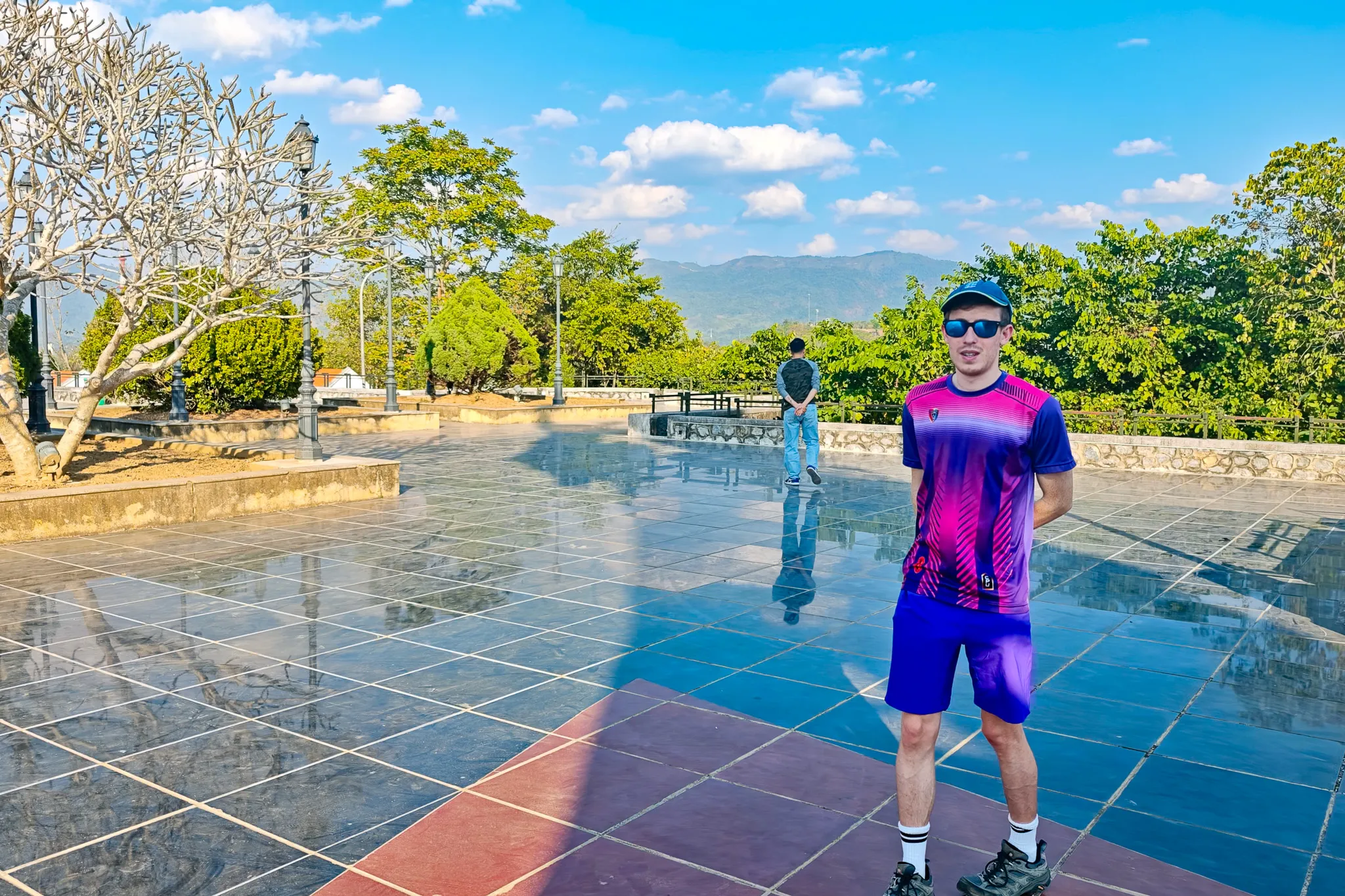 Traveller standing on the polished marble plaza at the Dien Bien Phu memorial with mountains in the background