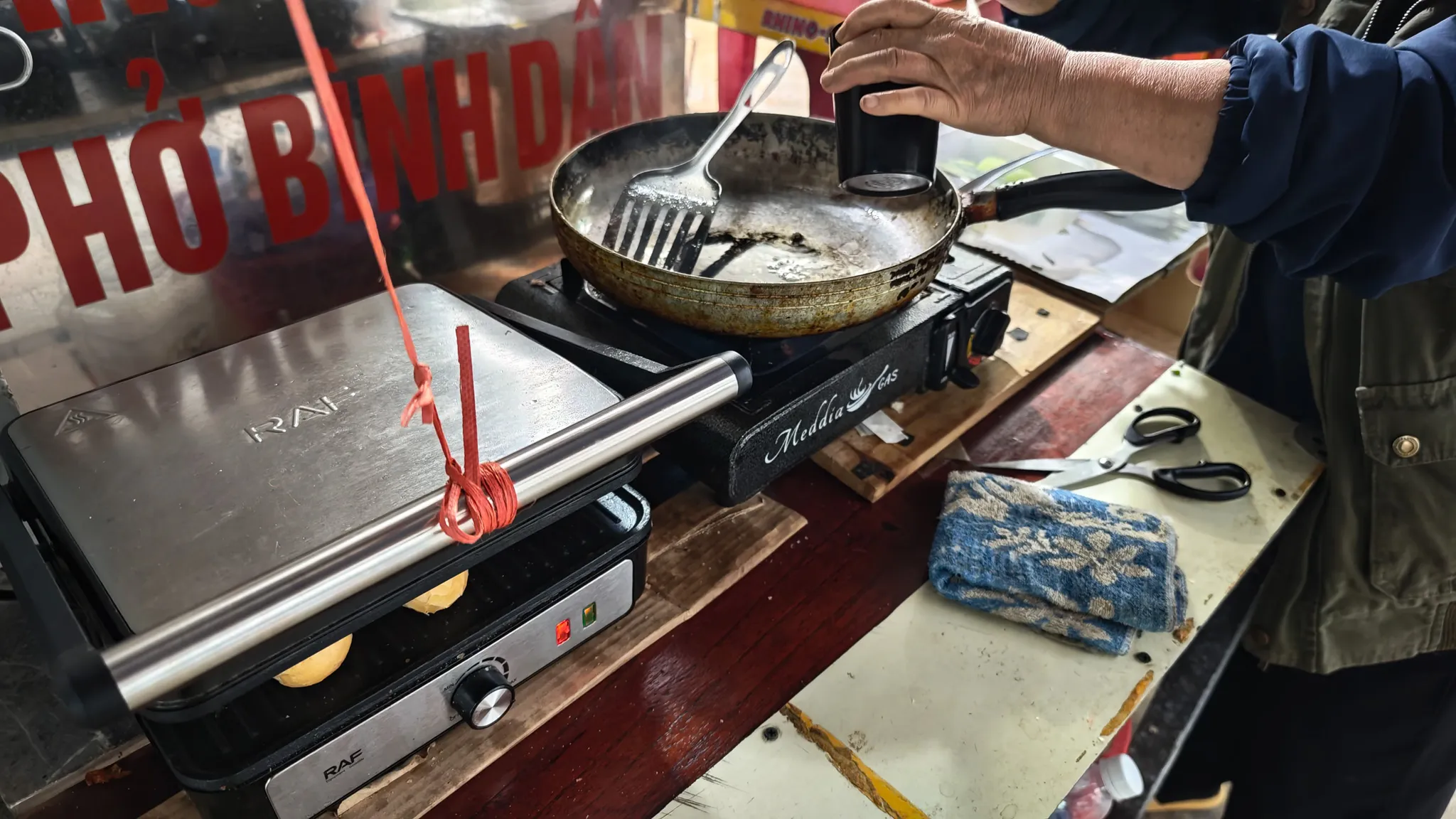 Street food vendor cooking on a portable gas stove and panini press at an early morning food stall in Dien Bien Phu, Vietnam