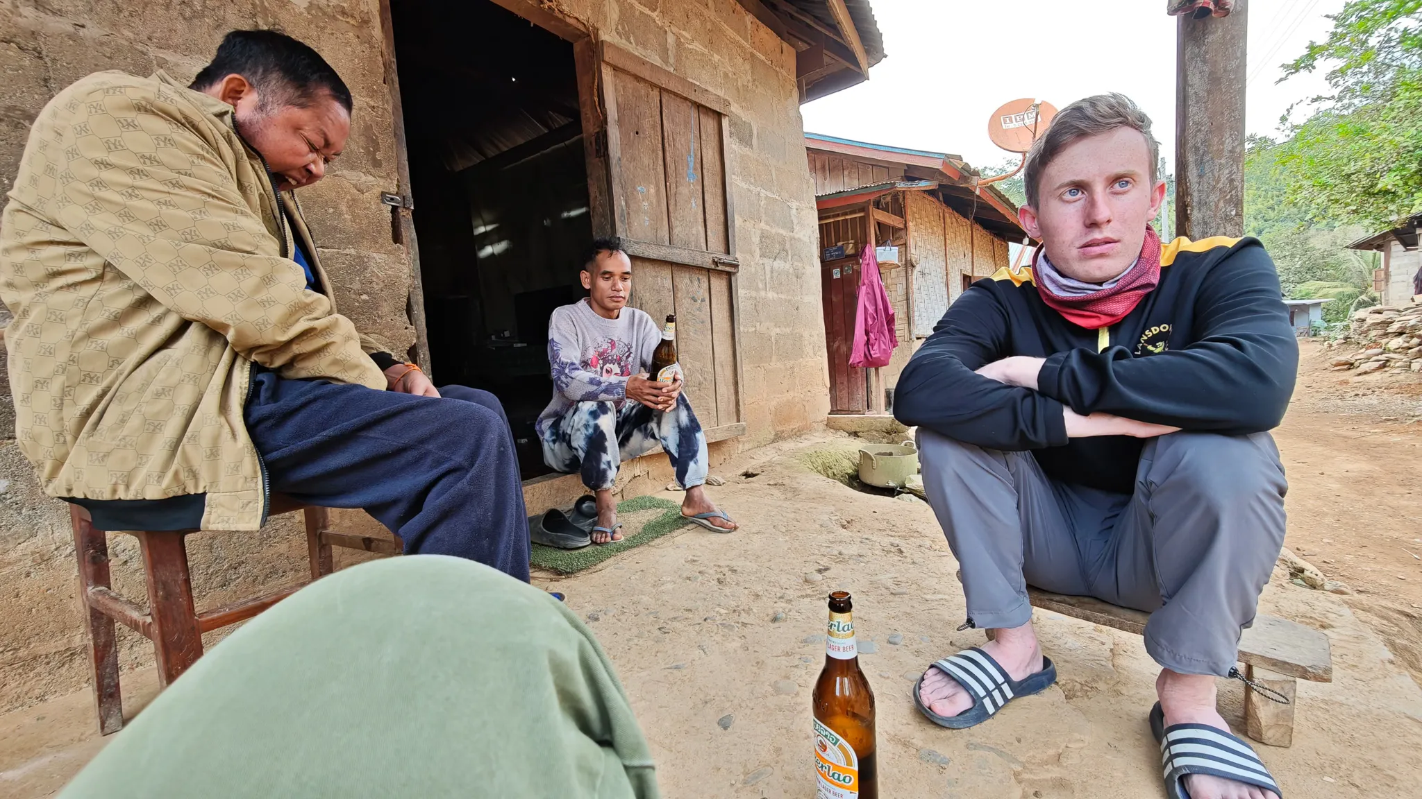 Traveller and local villagers drinking Beer Lao together outside a traditional house in Ban Haddean village on the Nam Ou