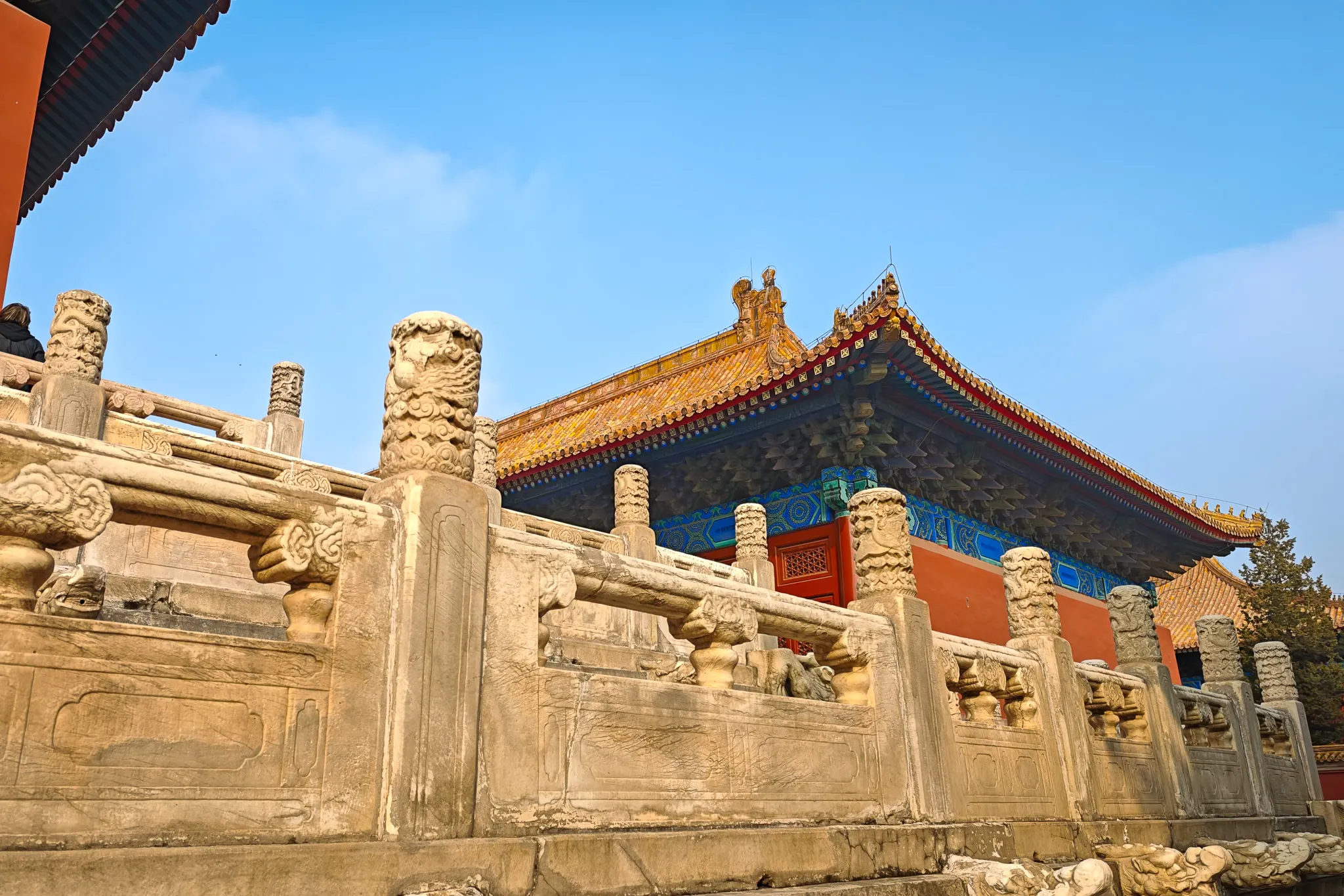 Carved marble balustrade and dragon pillars detail inside the Forbidden City with a golden-roofed hall behind