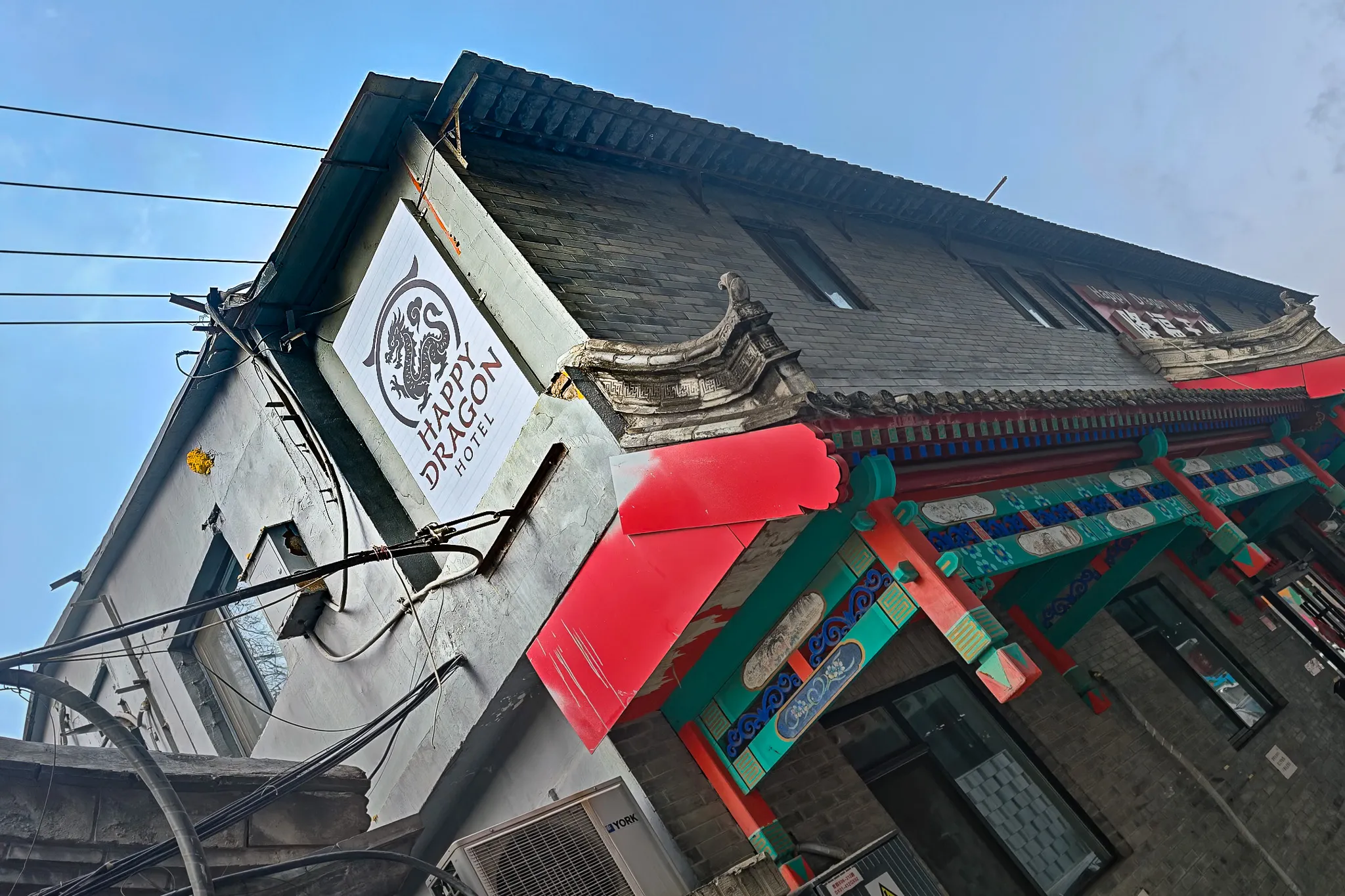Happy Dragon Hotel sign on a traditional grey brick building with a colourful Chinese gate entrance in a Beijing hutong