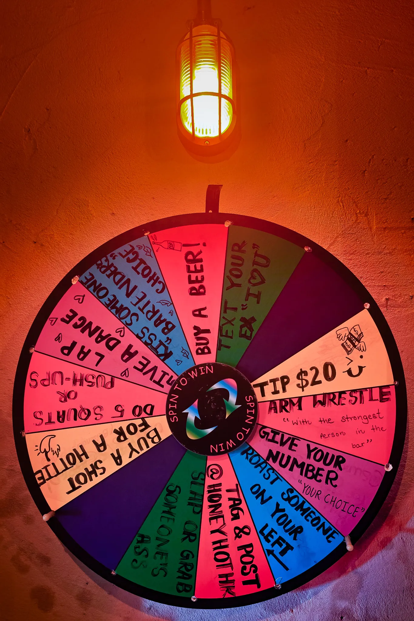 Colourful spin-to-win challenge wheel on a bar wall in Hong Kong with dares like arm wrestle and buy a beer