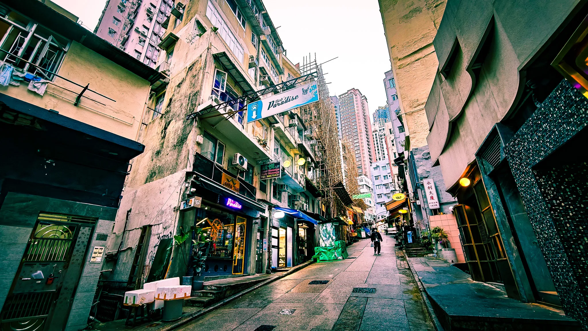Narrow street in Hong Kong SoHo area at dusk with bars, neon signs and tall apartment buildings rising above