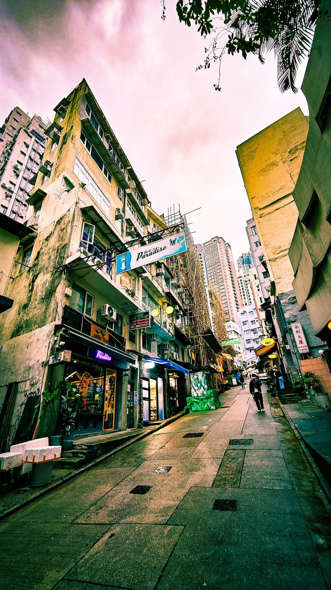 Portrait view looking up a narrow Hong Kong SoHo street at dusk with high-rise buildings and lit-up shopfronts