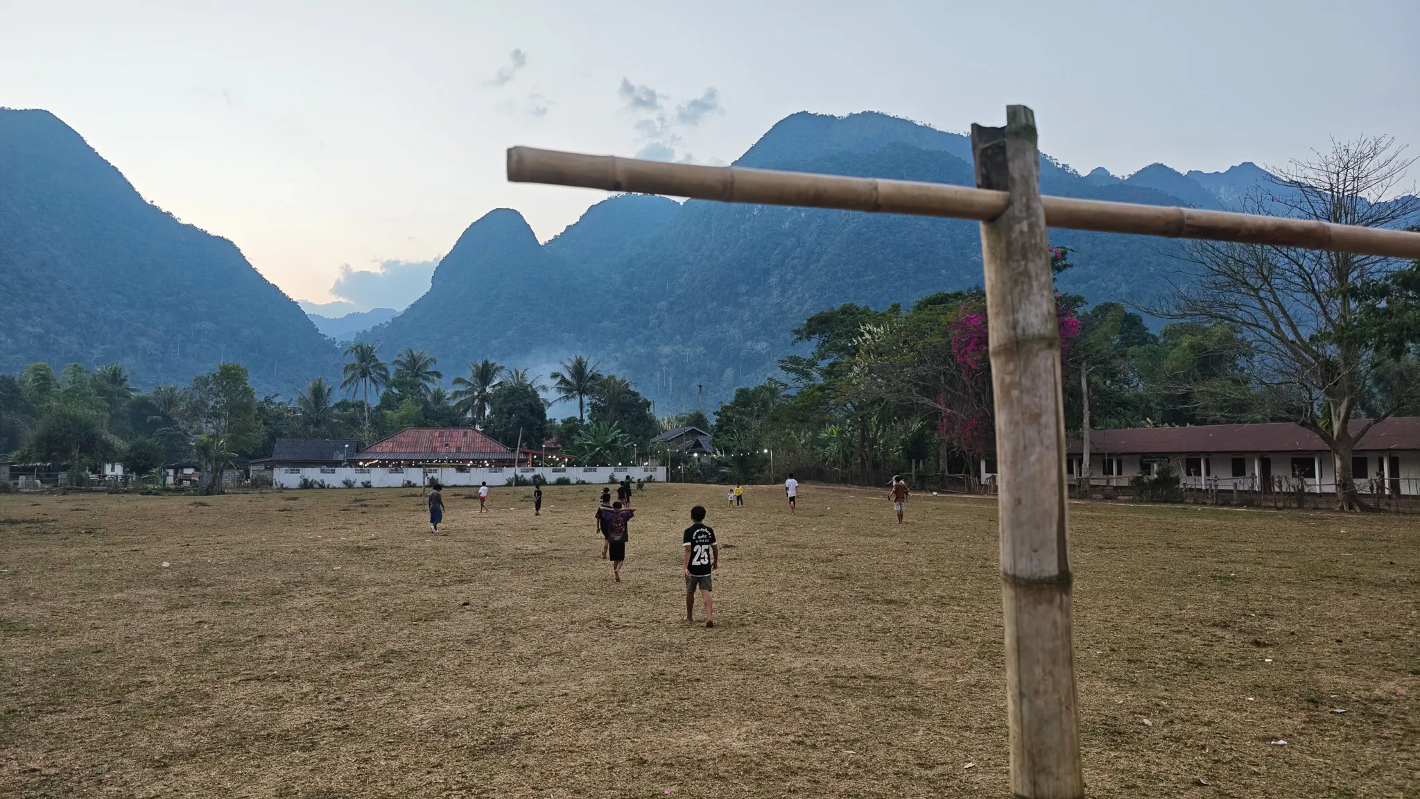 Children playing football on a dusty field with limestone karst mountains behind in Muang Ngoi, Laos