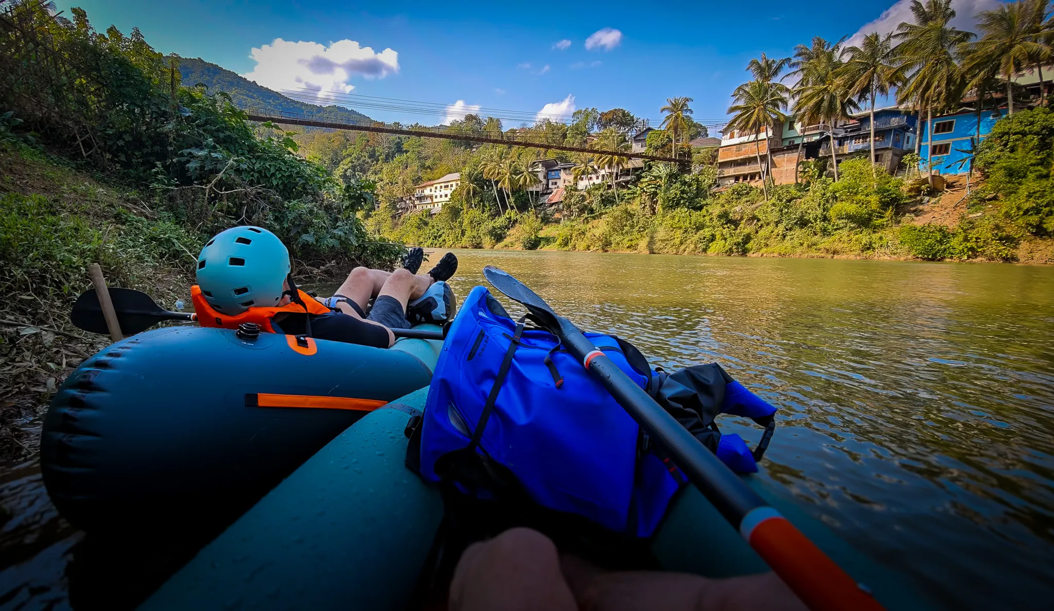 Close-up of three Lao children sitting on a bamboo raft in the Nam Ou river with a smiling packrafter in the background at Muang Khua