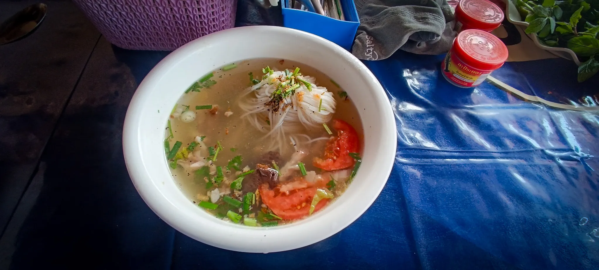 Close-up of steaming Lao noodle soup with spring onions and chilli flakes served at a Nong Khiaw noodle shop