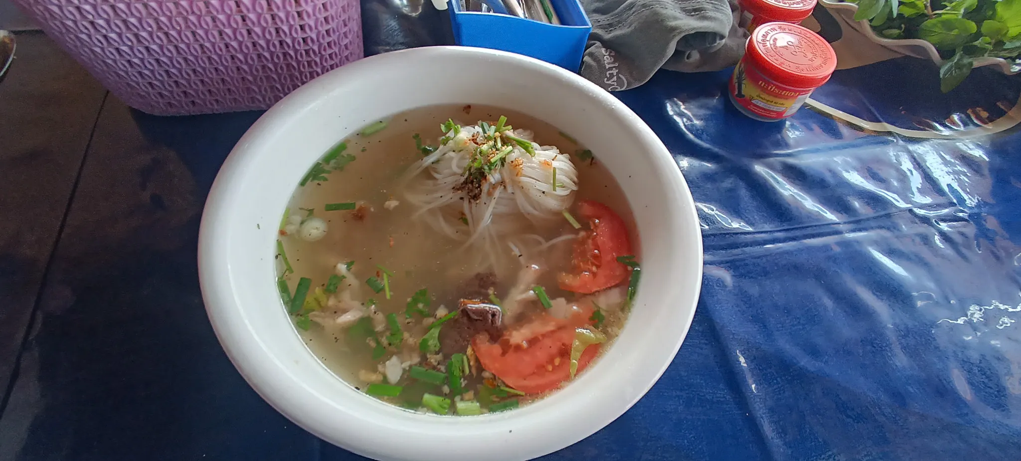 Bowl of authentic Lao noodle soup with rice noodles, tomato, herbs, and meat at a local restaurant in Nong Khiaw