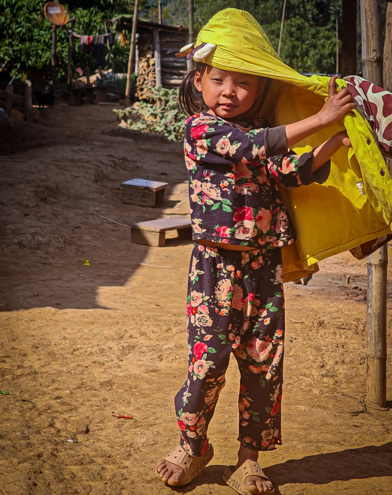 A young child in a floral outfit and yellow jacket standing in a Lao village along the Nam Ou river