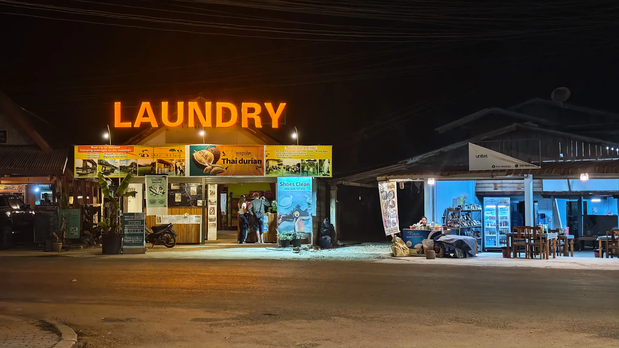 Neon laundry sign glowing above a tour agency and shops on the main street of Nong Khiaw at night