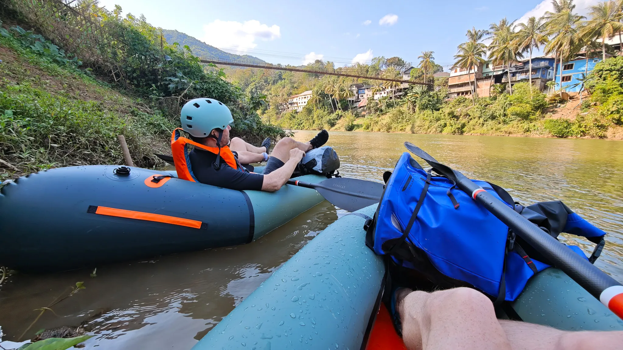 Three Lao children playing on a bamboo raft as a packrafter paddles by on the Nam Ou river near Muang Khua village