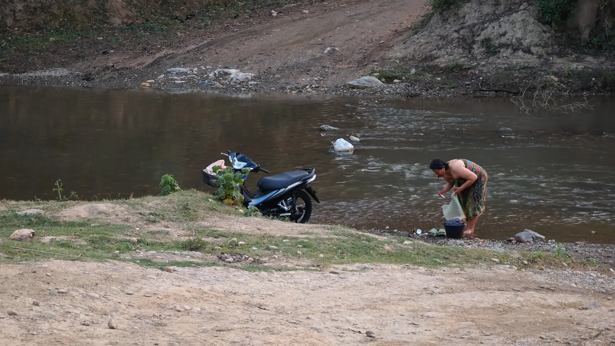 Local man washing by the Nam Ou river with a motorbike parked on the bank near Muang Ngoi