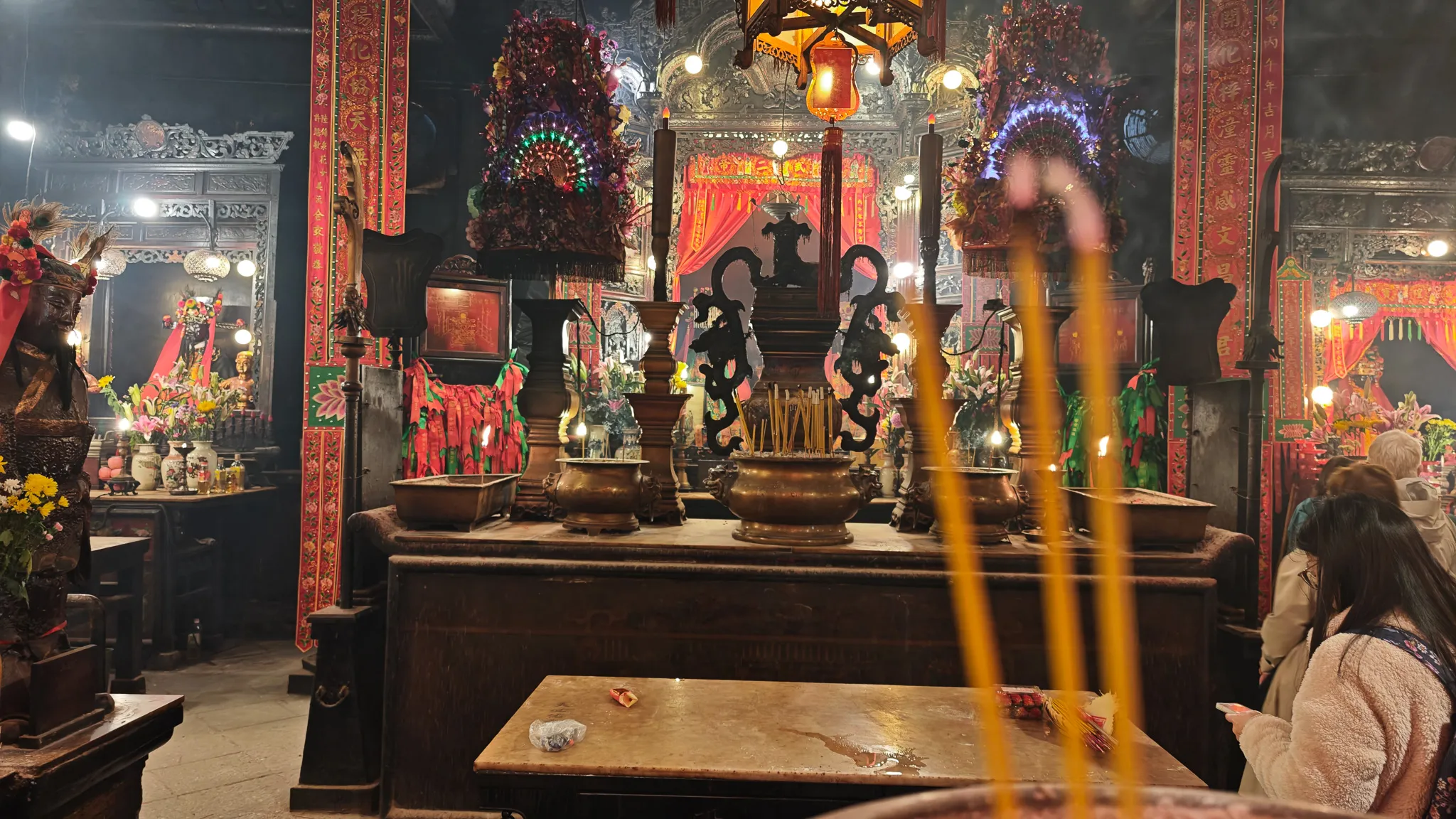 Wide view of the Man Mo Temple altar hall with worshippers, brass urns and incense smoke