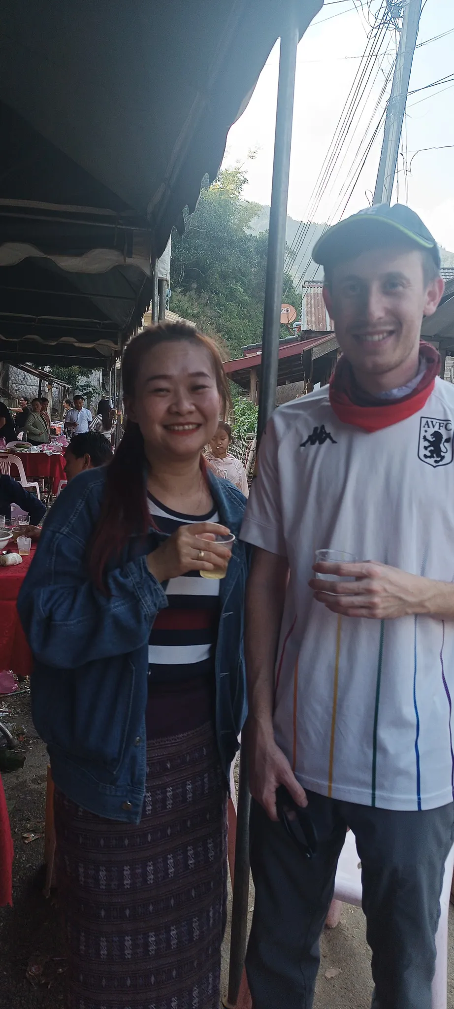 Traveller in Aston Villa shirt and local Lao woman smiling with drinks at a street party in Muang Khua