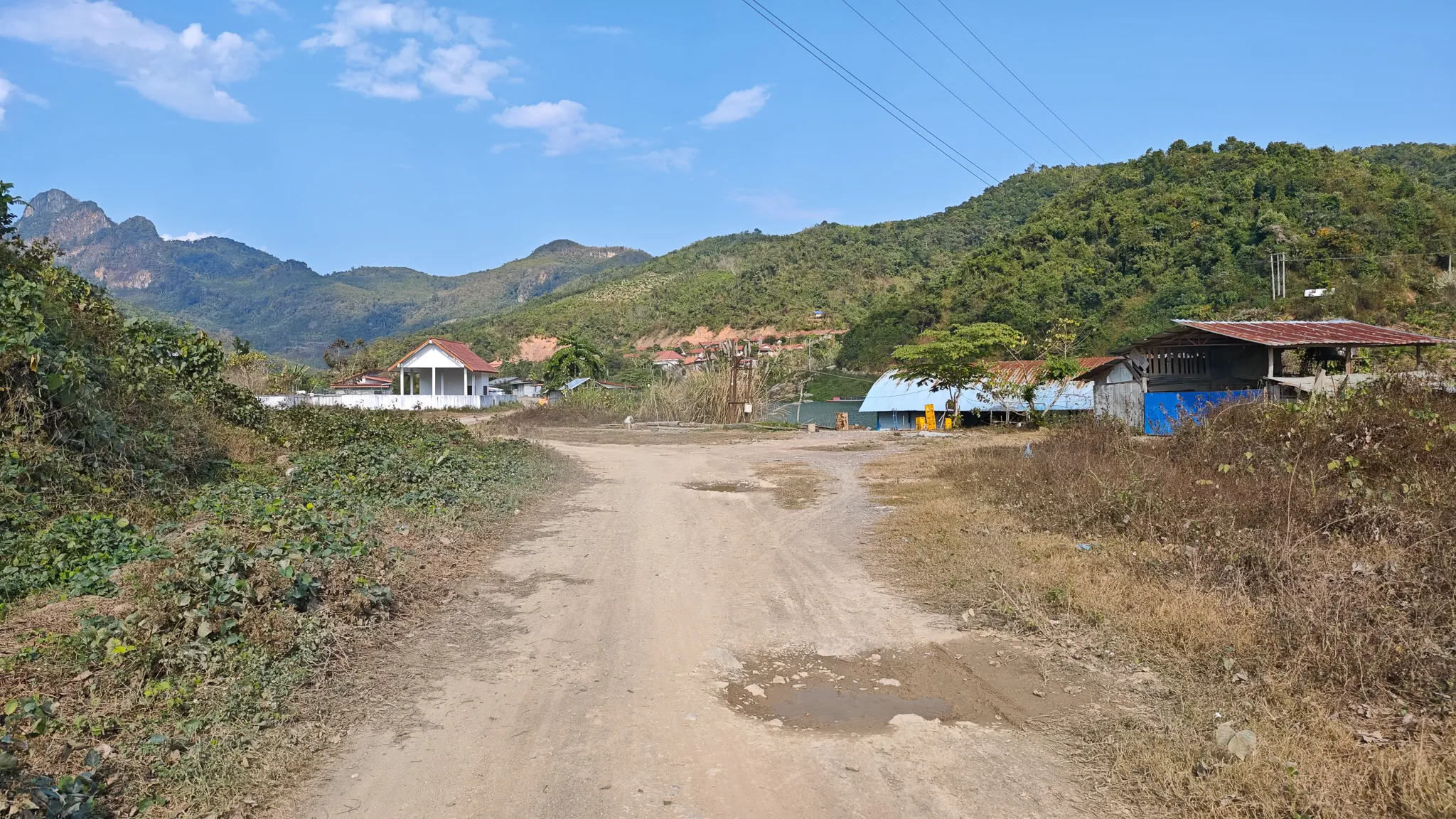 Dirt road leading into a small village below a Nam Ou dam, with karst mountains rising in the background