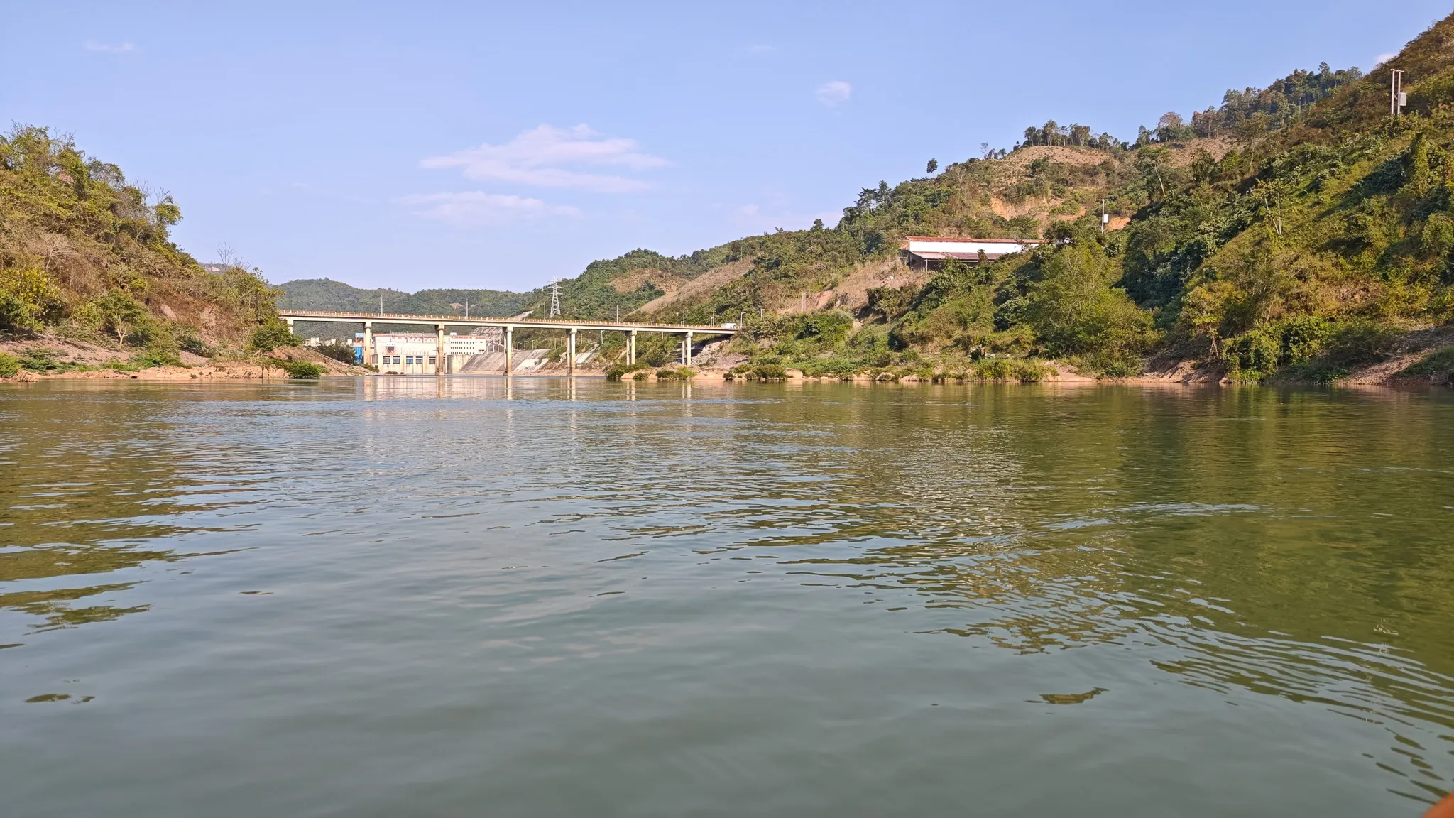 First Nam Ou hydroelectric dam seen from the water while approaching by packraft, with forested hills on both sides