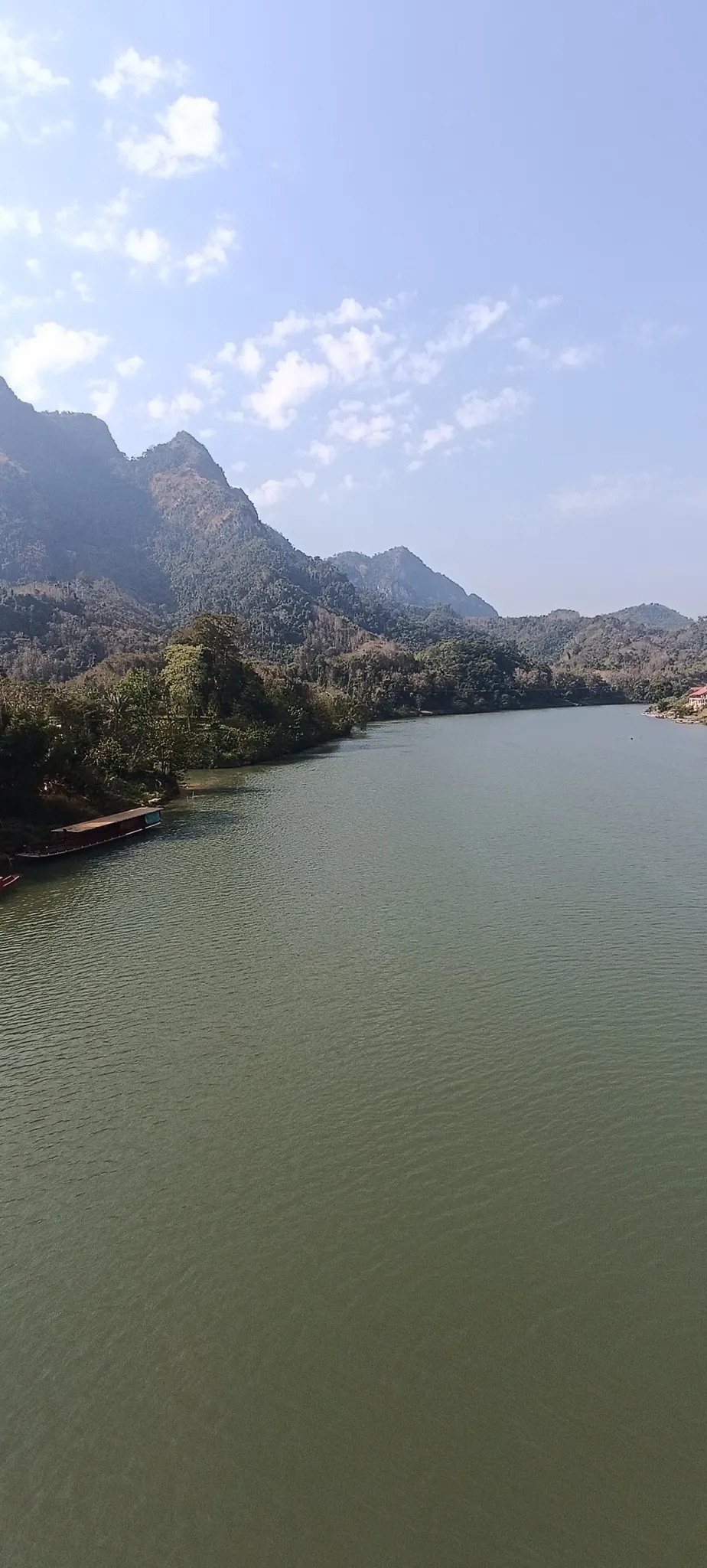 Portrait view of the Nam Ou river flowing past karst mountains with a longboat moored on the bank