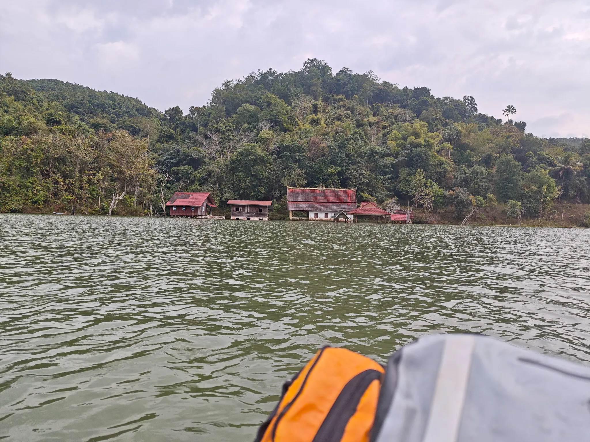 Red-roofed riverside buildings viewed from a packraft on the Nam Ou river with jungle-covered hills in the background