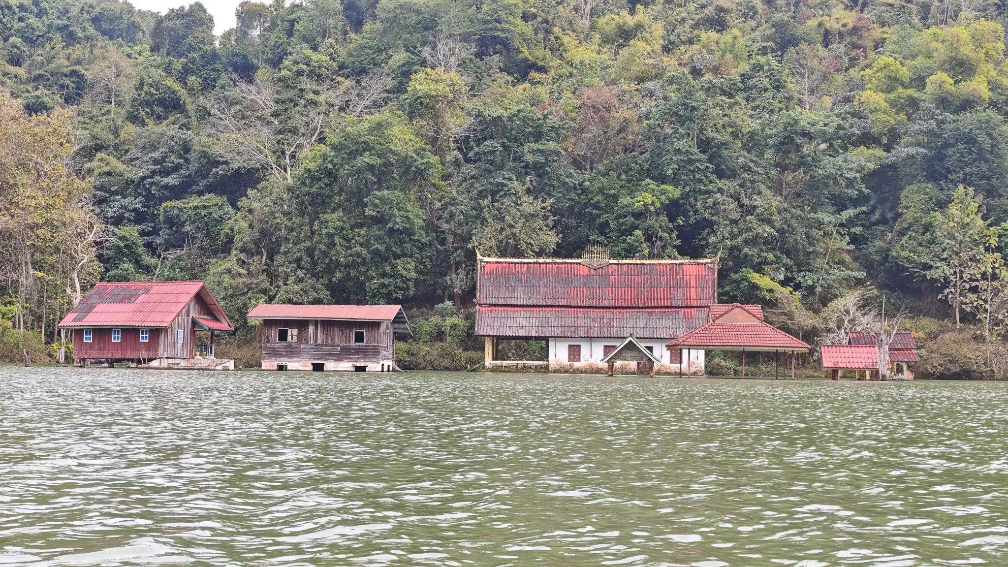 Wide view of red-roofed village buildings backed by forested hills on the Nam Ou river in Laos