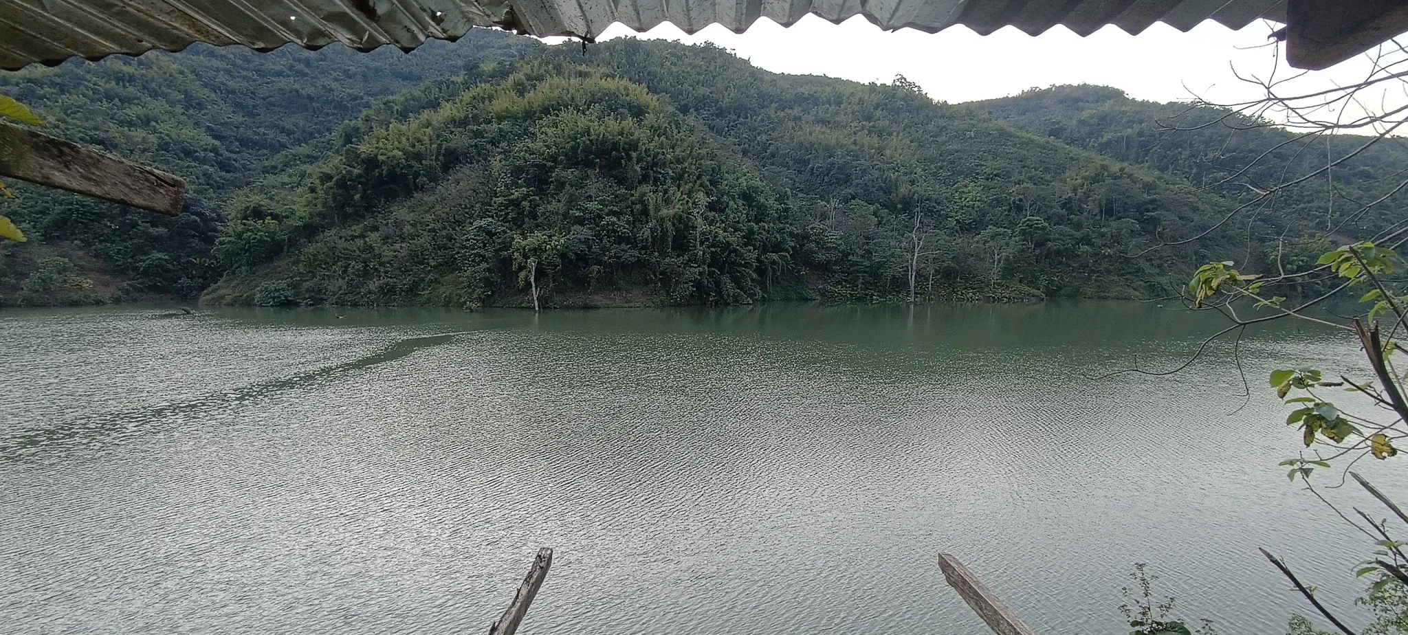 View of the Nam Ou river and jungle-covered hills from under the corrugated roof of an abandoned riverside shelter