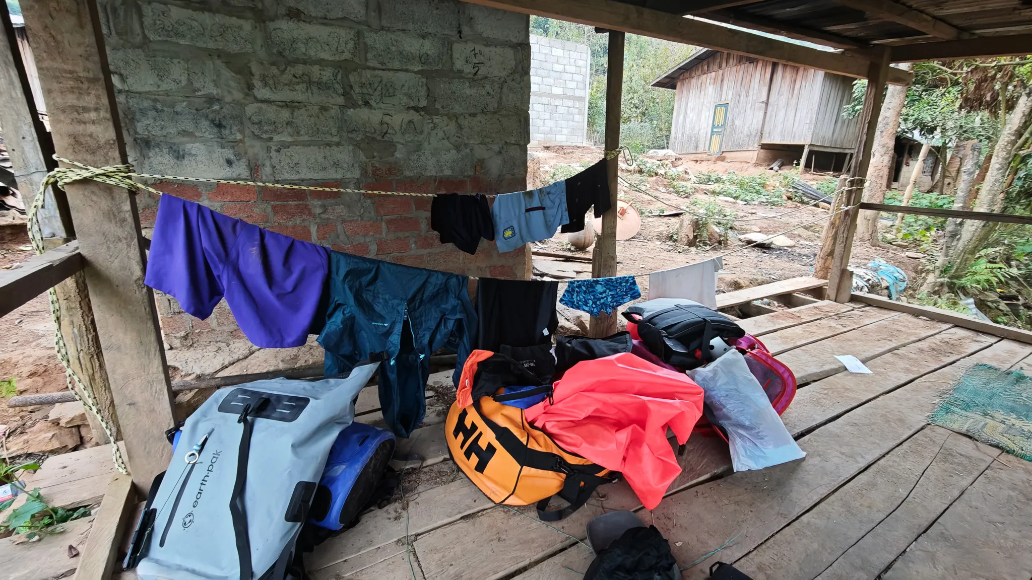 Packrafting gear and dry bags drying under a wooden shelter at a riverside village on the Nam Ou, Laos