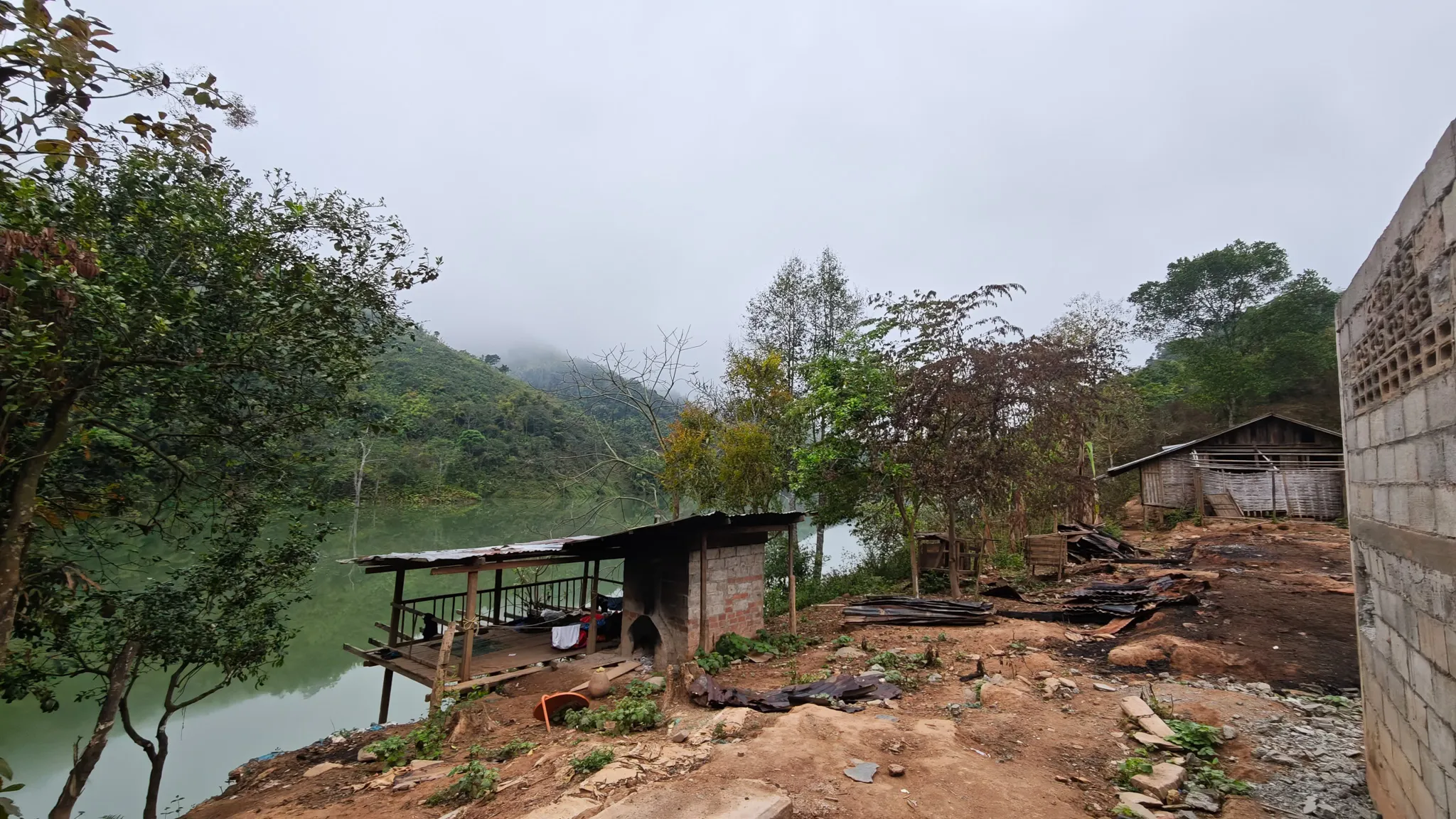 Riverside village with a wooden platform overlooking the still green waters of the Nam Ou, surrounded by misty hills