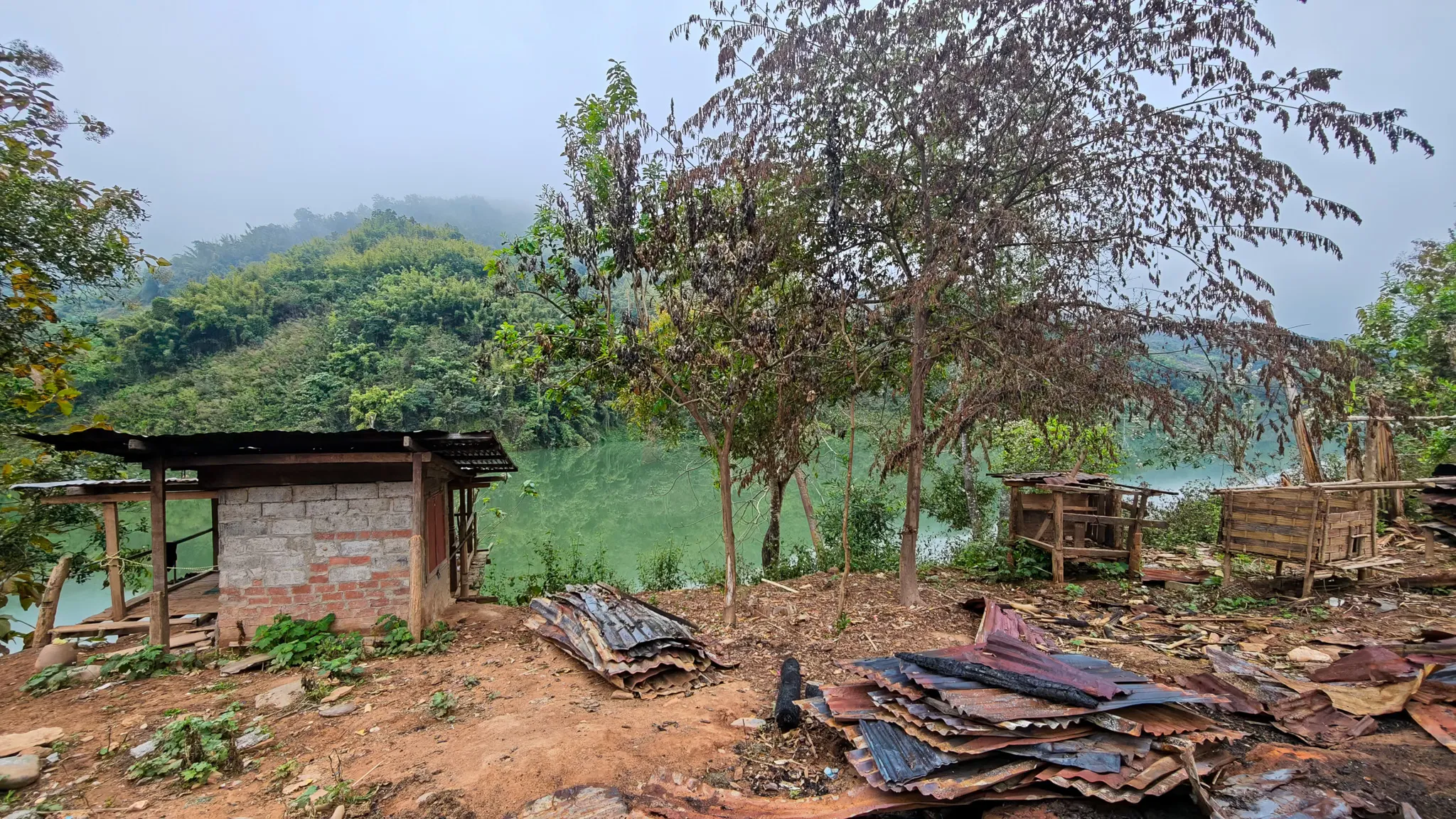 Trees and a small shelter on the bank of the Nam Ou river on a hazy morning in northern Laos