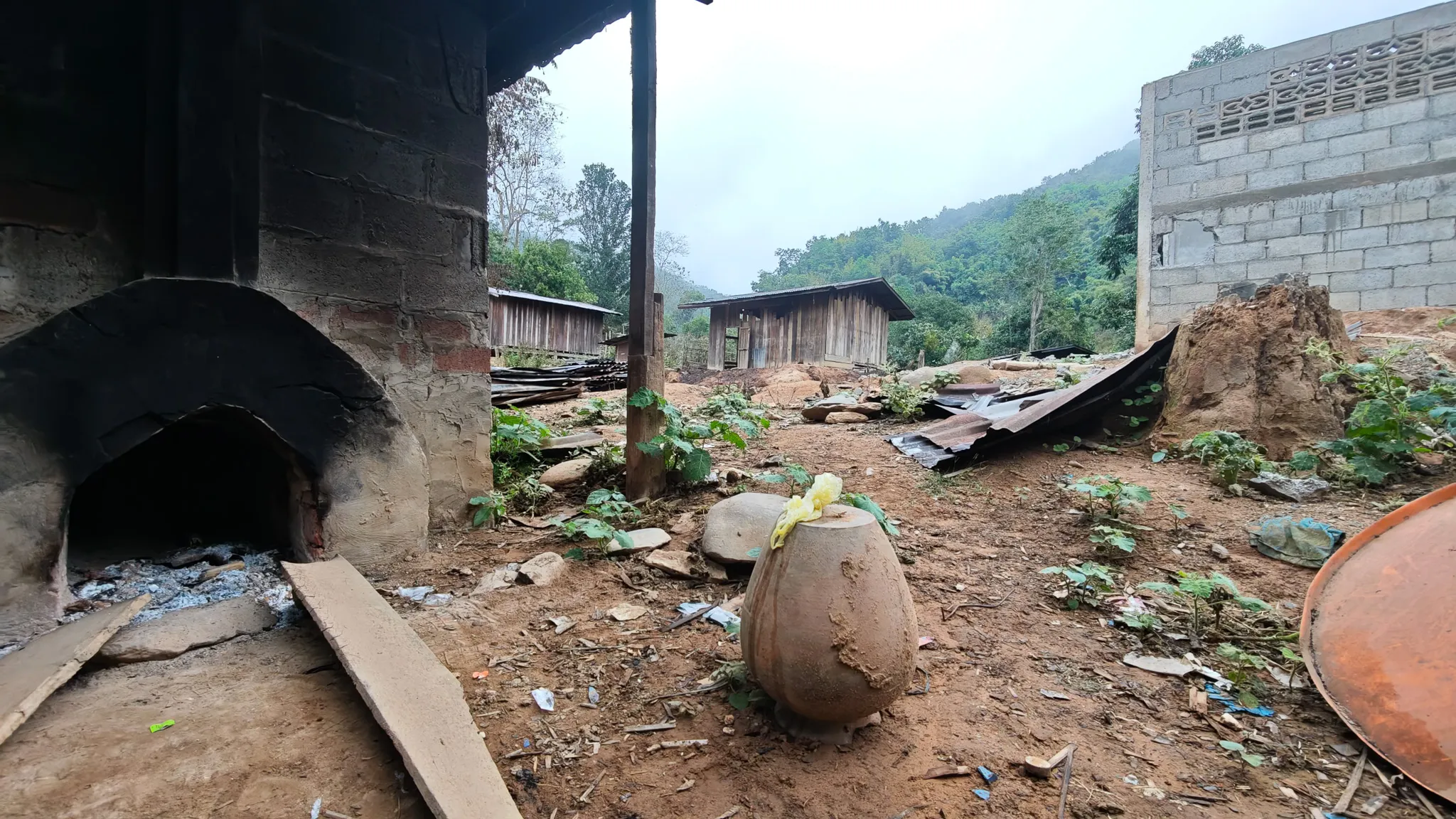 Traditional clay oven and pottery jar in a rural village along the Nam Ou river with misty mountains behind