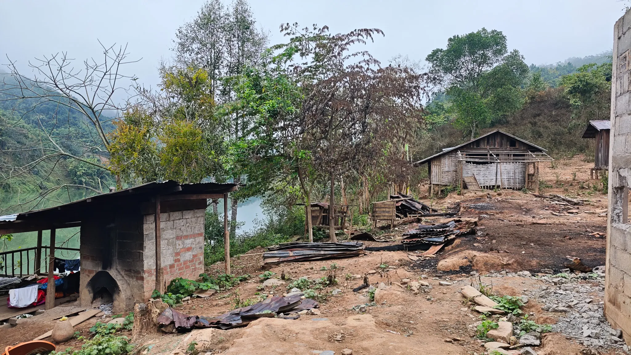 Village houses with wooden walls and corrugated roofing near the Nam Ou river, with dense jungle-covered hills behind