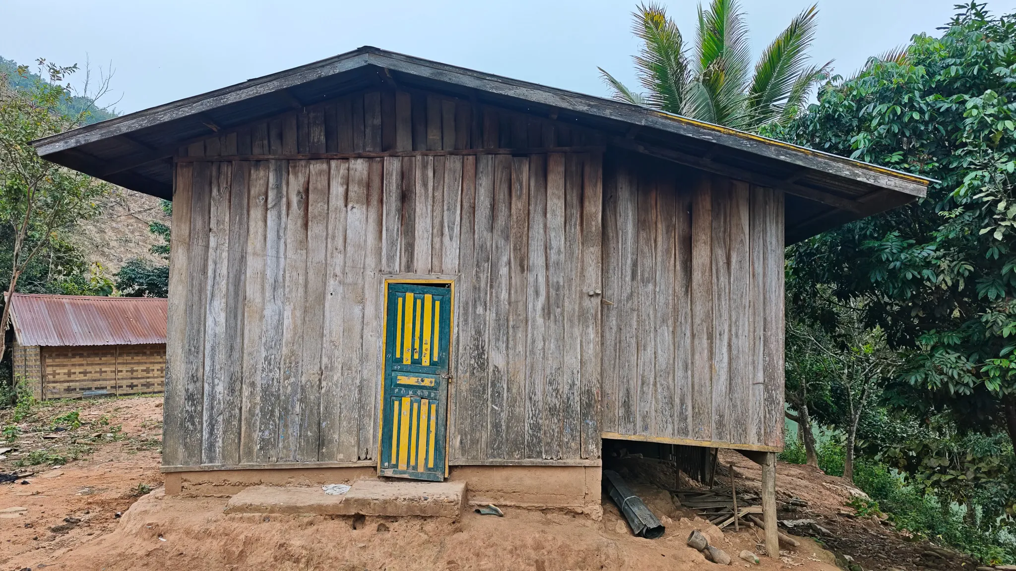 Weathered wooden house with a colourful yellow and green door in a village along the Nam Ou river