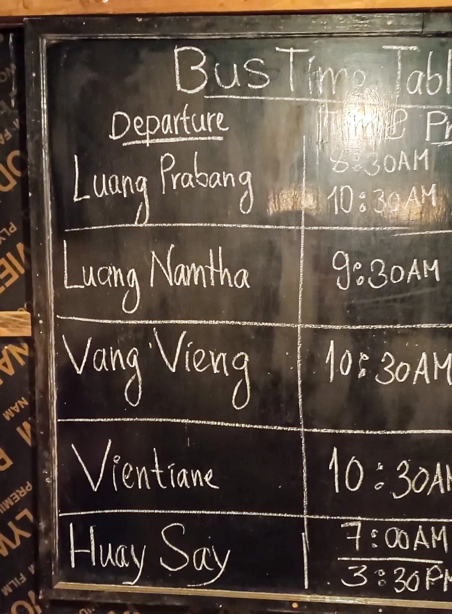 Chalkboard bus timetable showing departures from Nong Khiaw to Luang Prabang, Vang Vieng, Vientiane, and Huay Say
