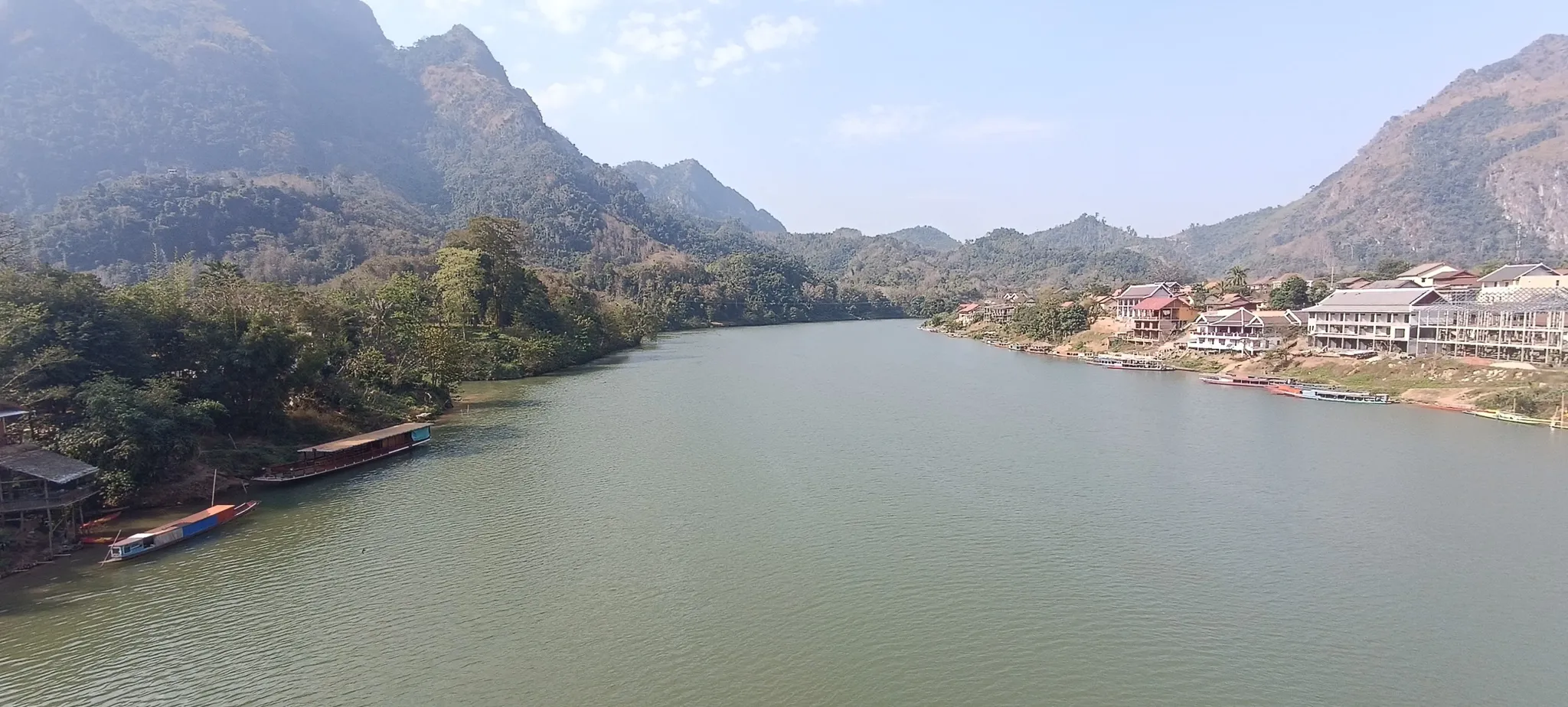 Downstream view of the Nam Ou river from Nong Khiaw bridge with longboats and riverside buildings