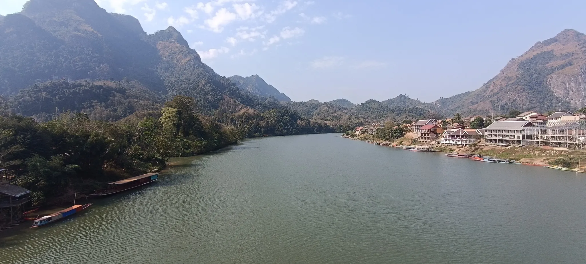 Nong Khiaw riverside town with longboats and hotels backed by karst mountains and blue sky