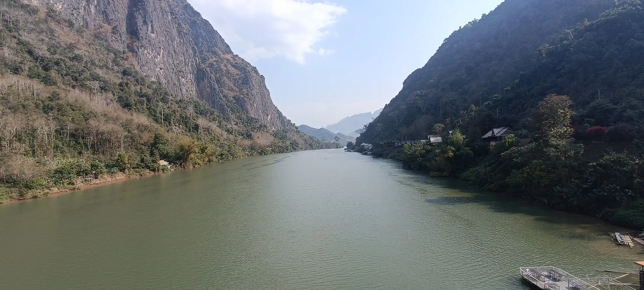 Looking upstream along the Nam Ou river at Nong Khiaw with a sheer cliff face rising from the water