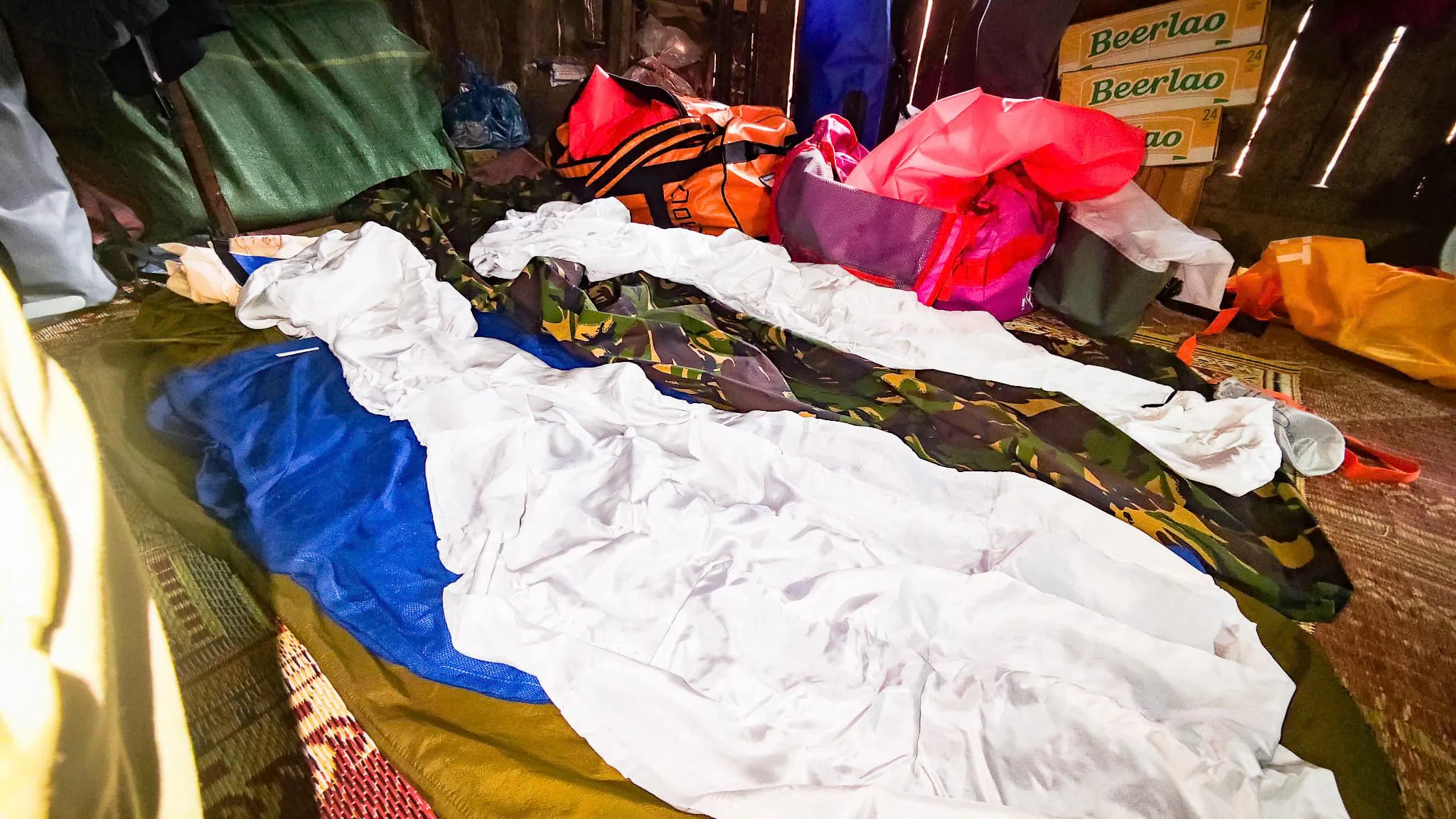 Packrafting gear and dry bags spread out to dry on the floor of a village house with Beerlao cartons nearby in Ban Haddean