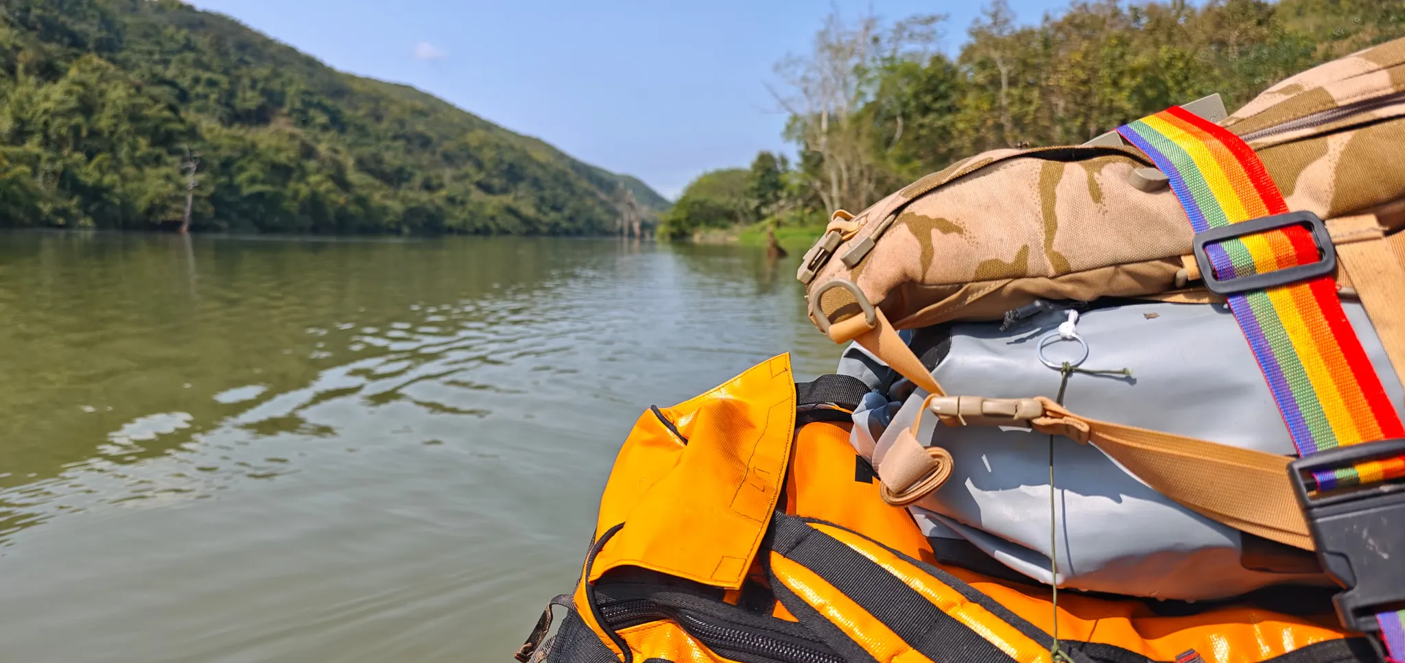 View from a packraft showing orange life jacket and camo dry bag with the calm Nam Ou river stretching ahead between forested hills