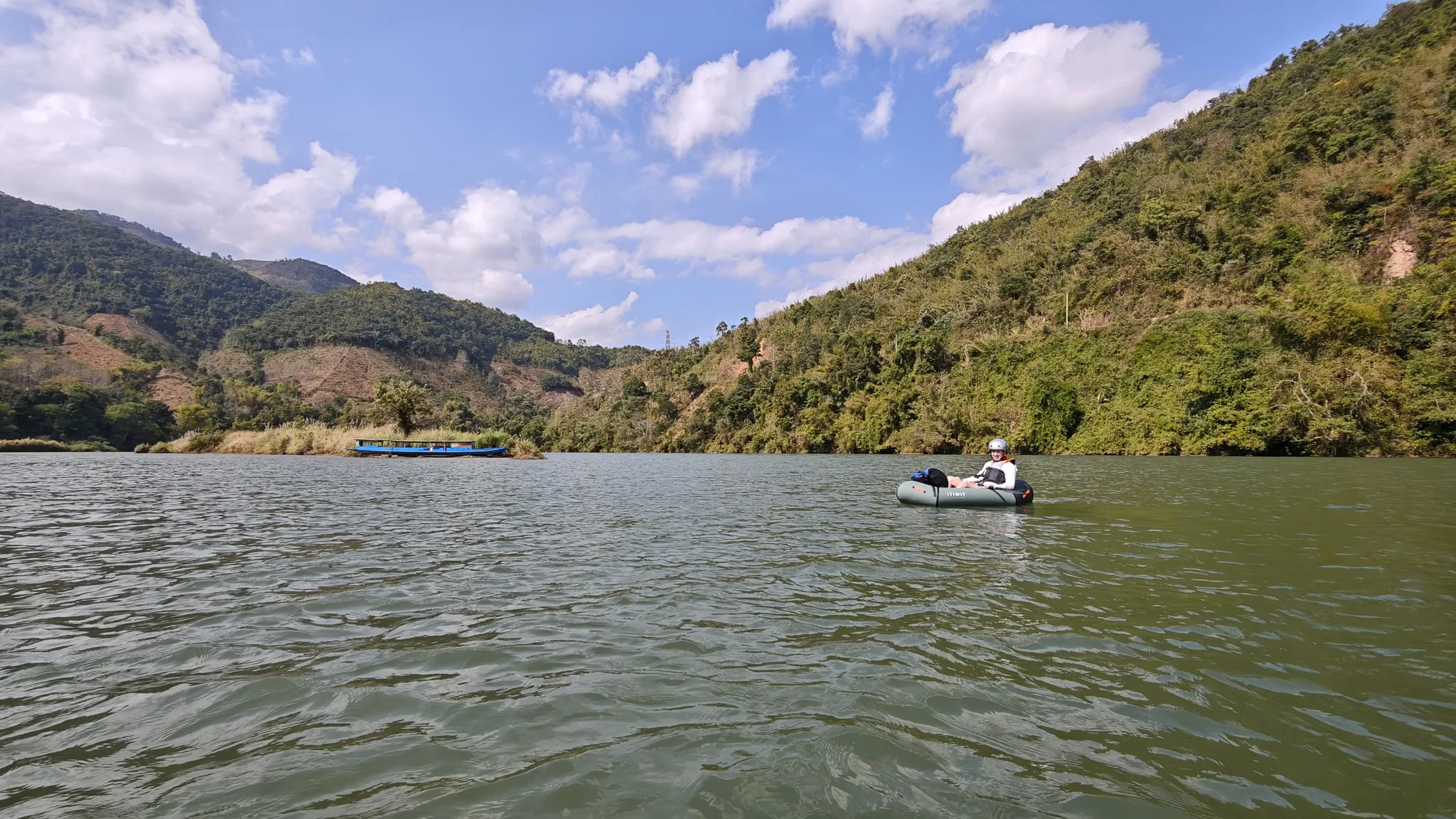 Packrafter paddling on the wide Nam Ou river near Muang Khua with a traditional longboat and forested mountains in the background