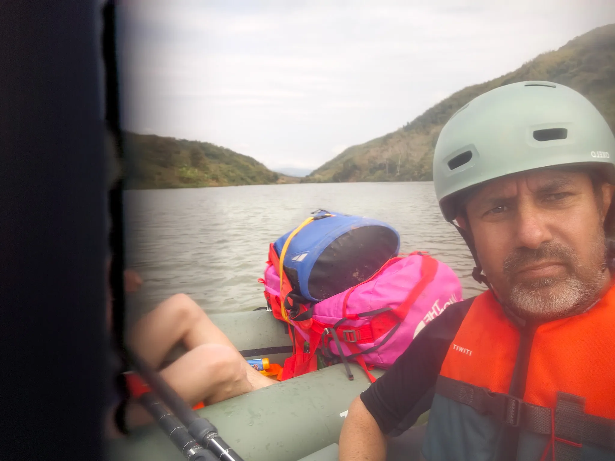 Selfie from a packraft on the Nam Ou river showing a paddler in helmet and orange life jacket with gear and forested hills behind